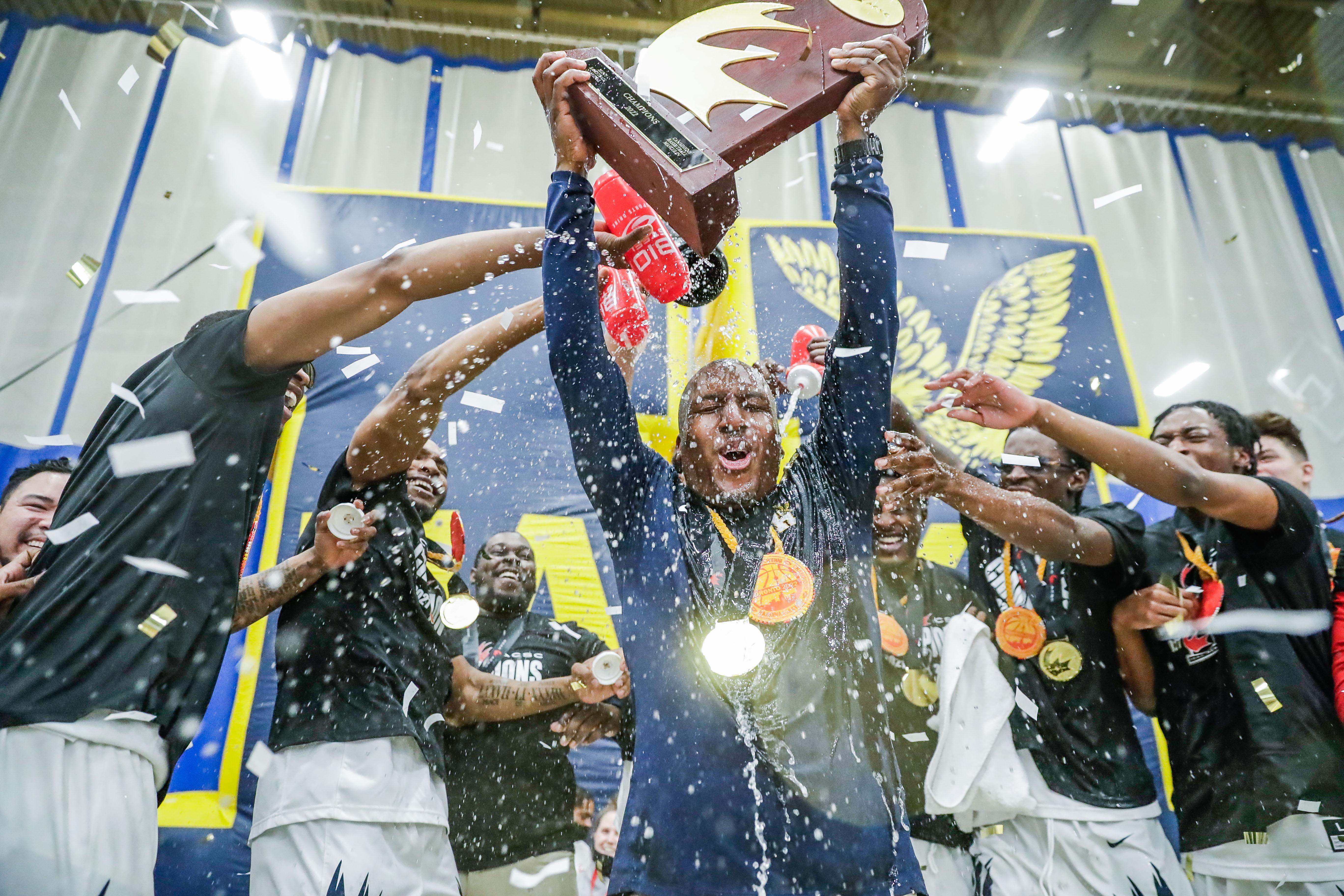 Athletes cheer and spray a person with water as that person lifts a trophy above their head.