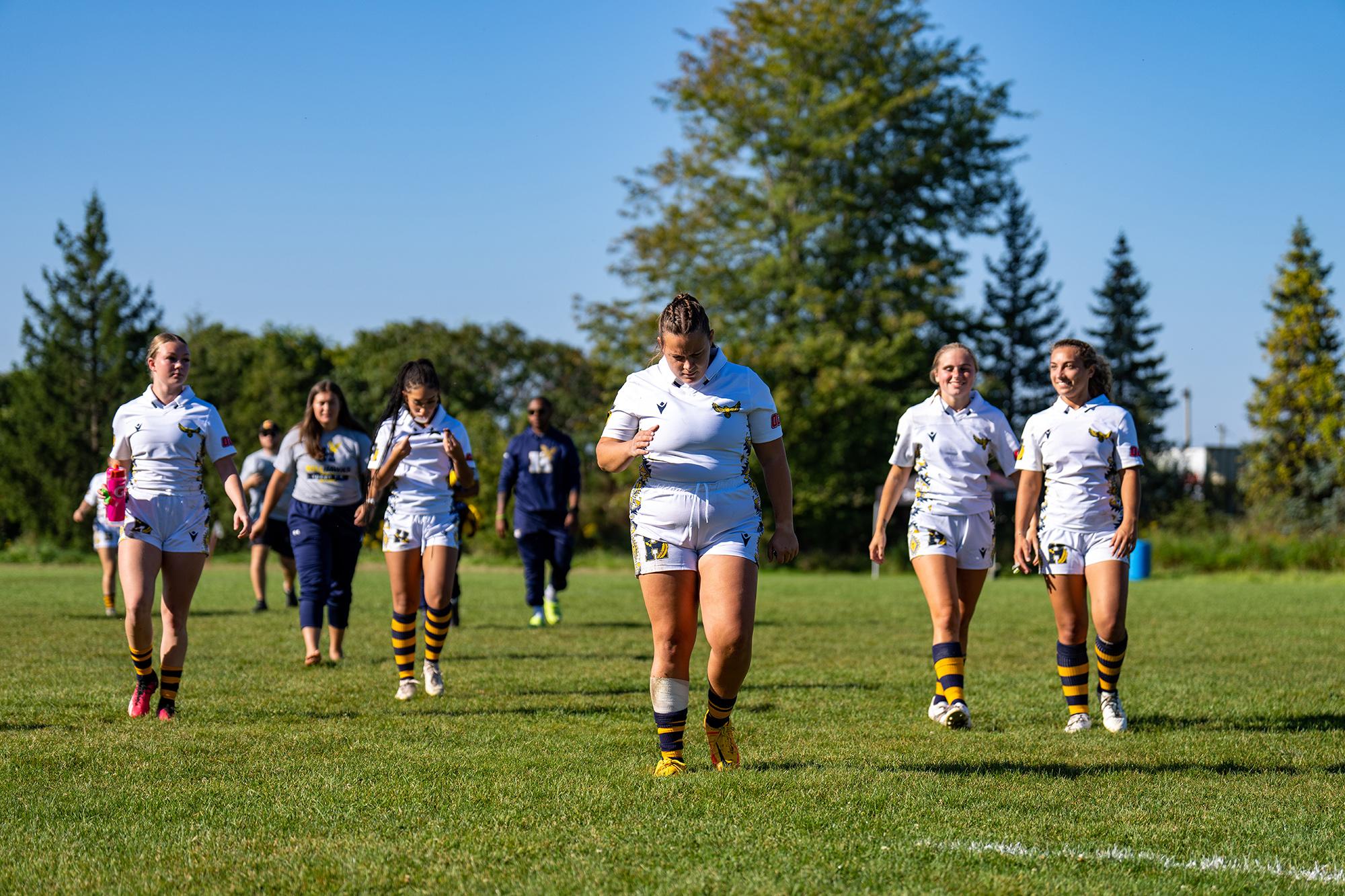 A group of athletes wearing Humber rugby jerseys walk across a field.