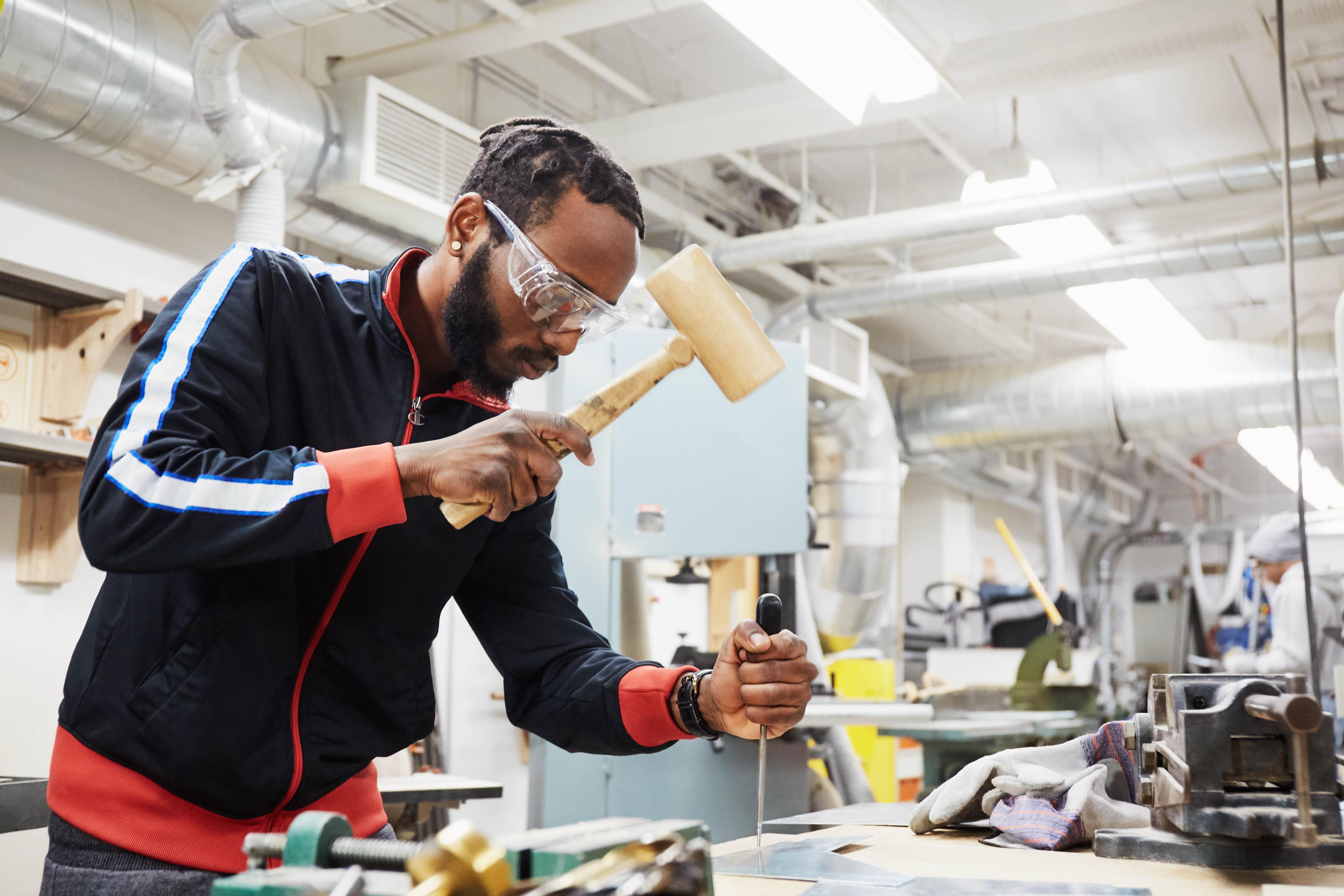 a student wearing safety goggles uses a mallet on a board in the Centre for Skilled Trades and Technology