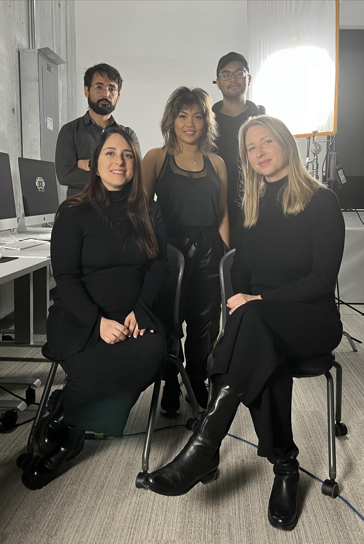 A group of five people pose for a photo. Two are sitting on chairs in the front.