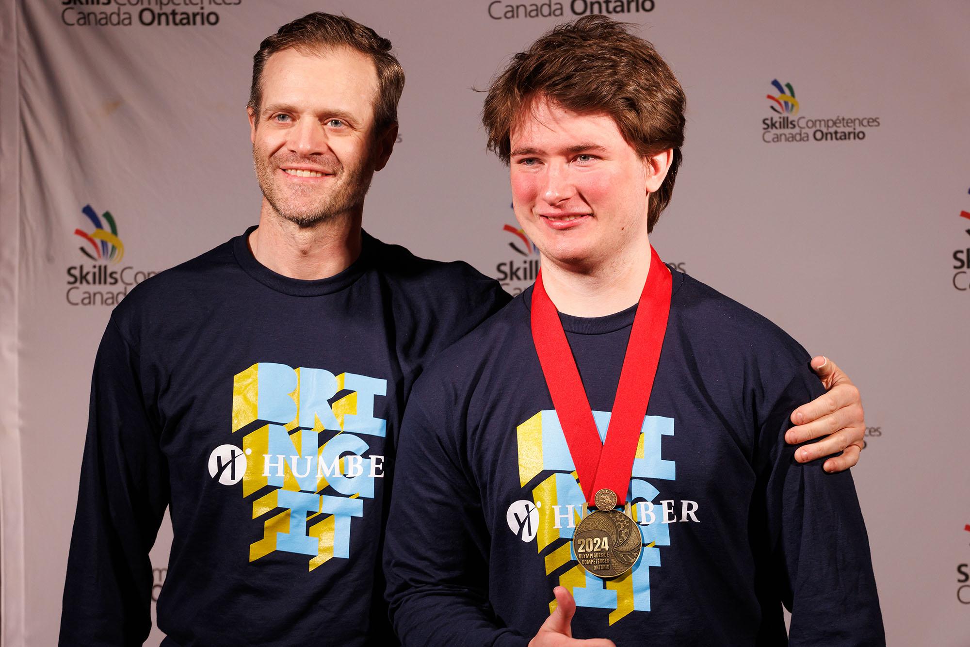 Two people wearing Humber shirts, one of whom is wearing a medal around their neck.