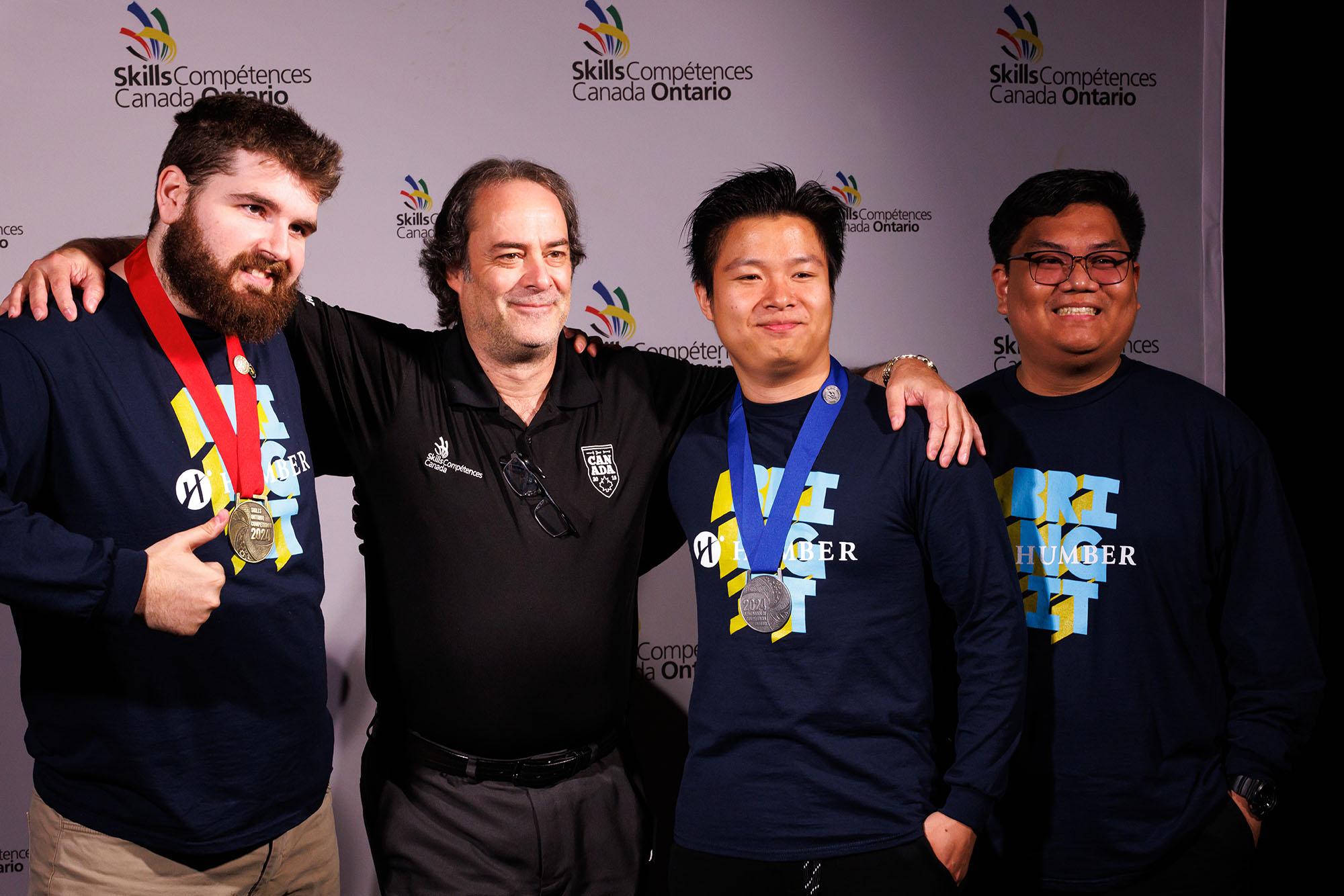 Four people stand together. Three a wearing Humber shirts. Two have medals around their necks.
