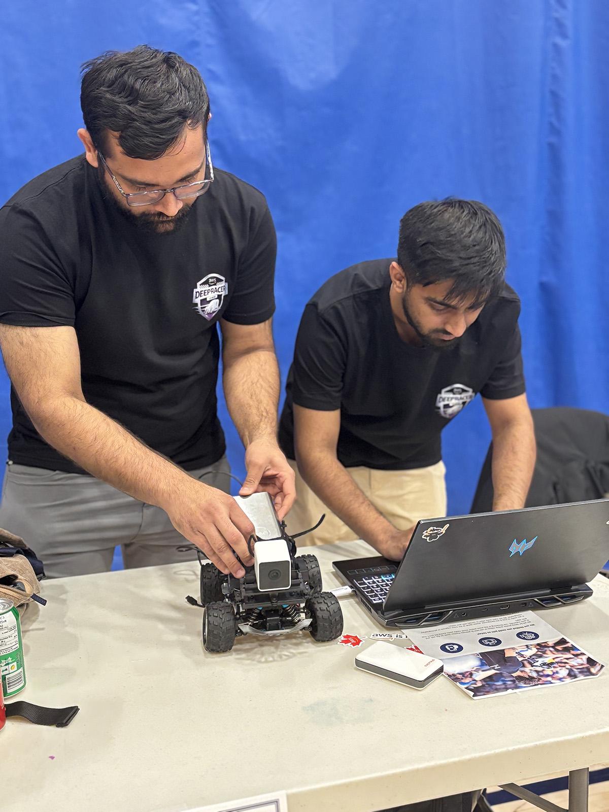 A person is working on a scale race car while another person works on a laptop.