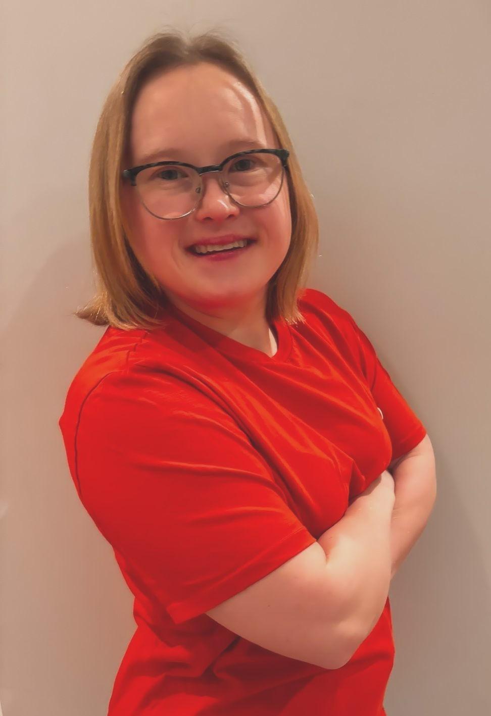 A smiling person stands with their arms crossed.