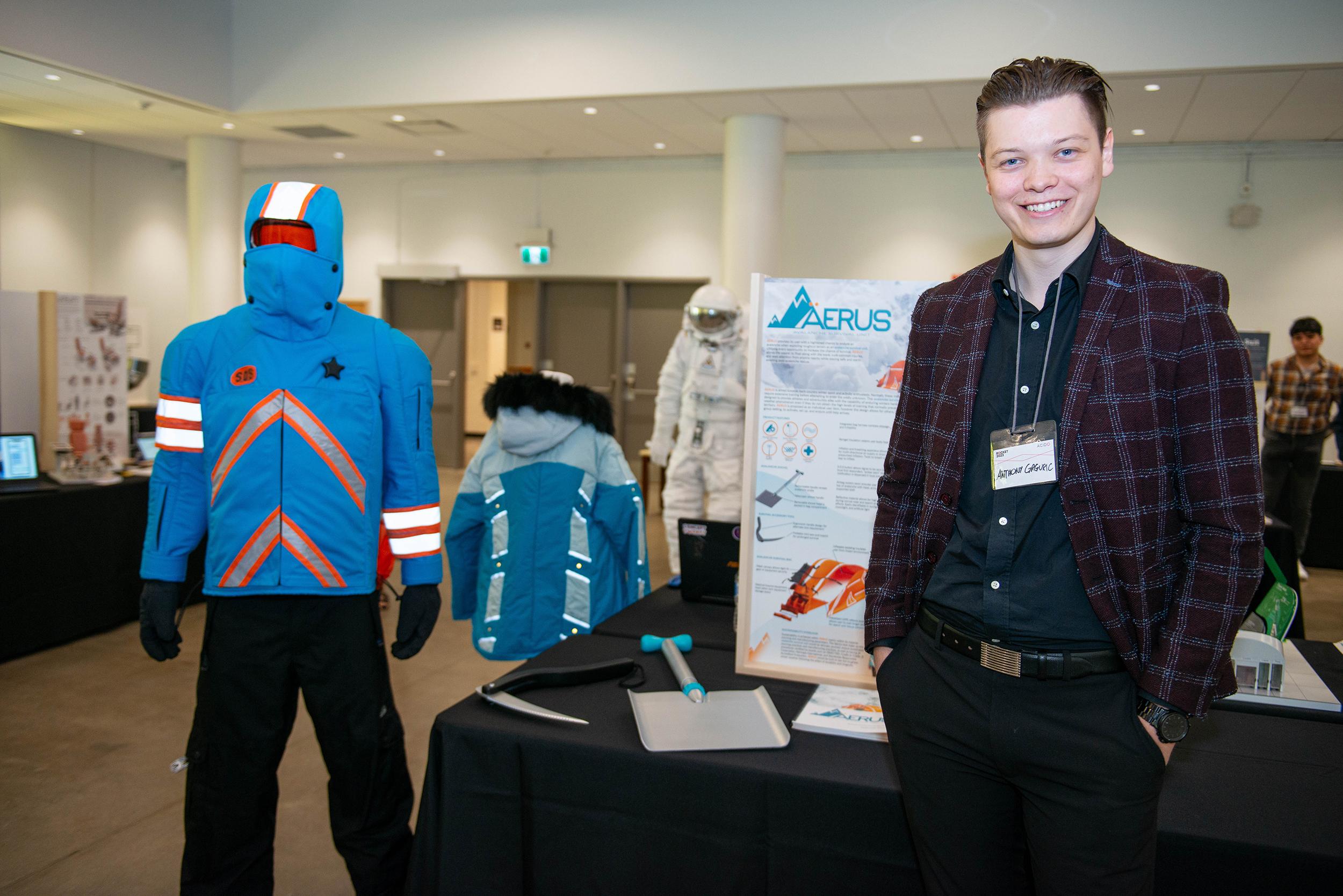 A person stands before a table that has a display on it that reads Aerus. A mannequin wearing winter clothes is next to it.