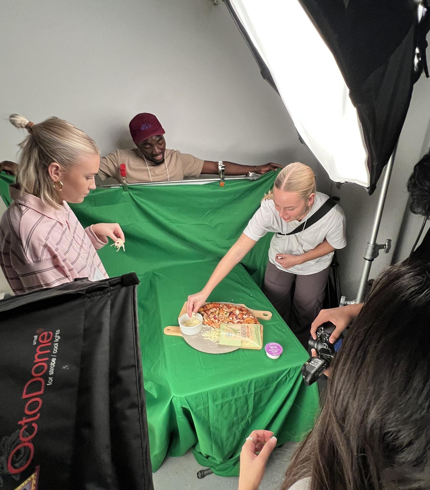 Several people on the set of a photoshoot arrange food on a table.