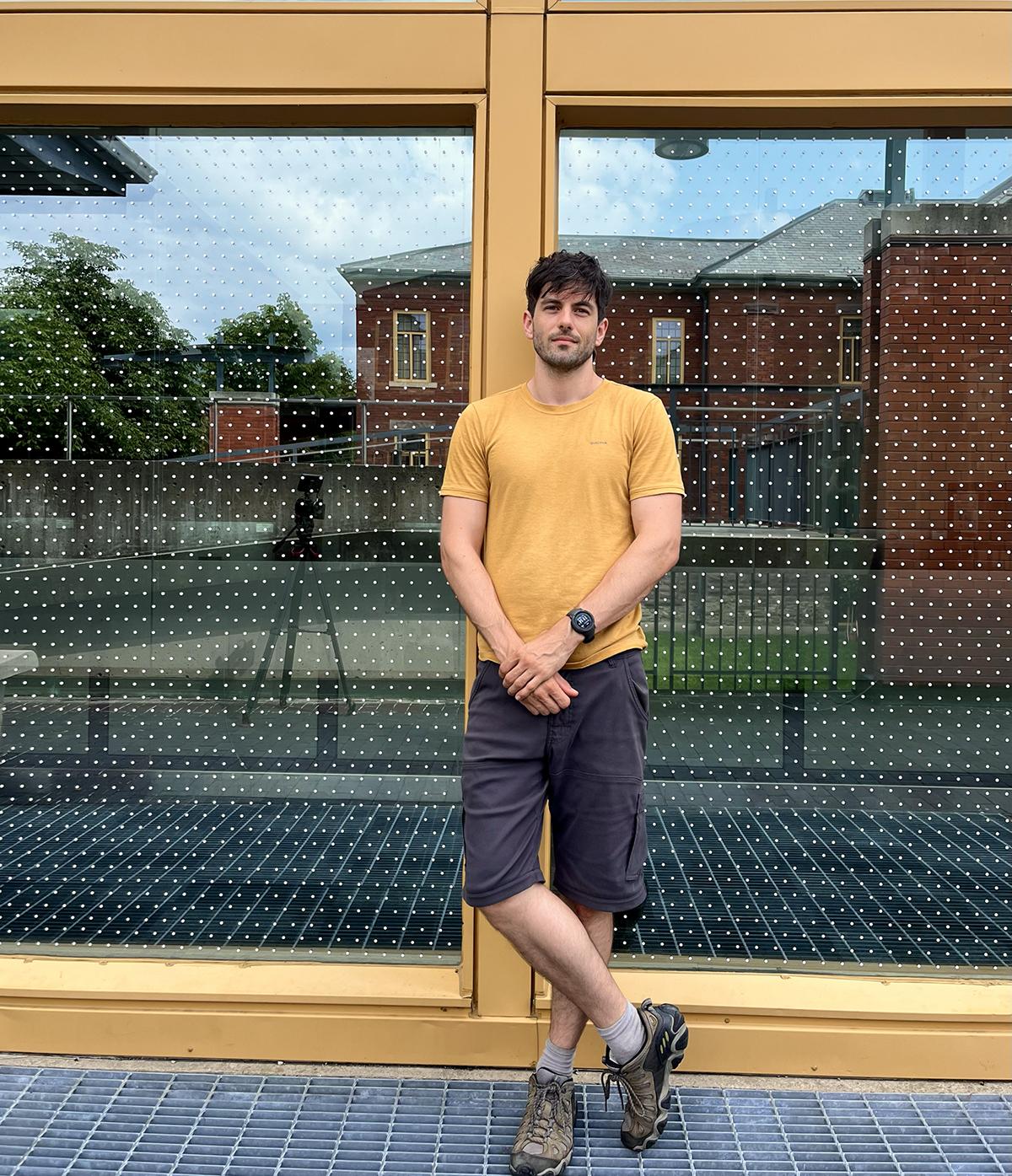 A person stands in front of a window with bird-deterrent dot markers on it.