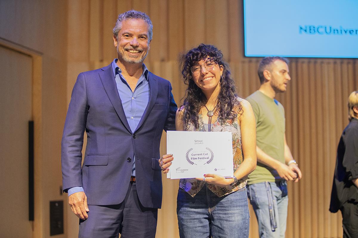 Two smiling people stand together and one is holding a certificate.