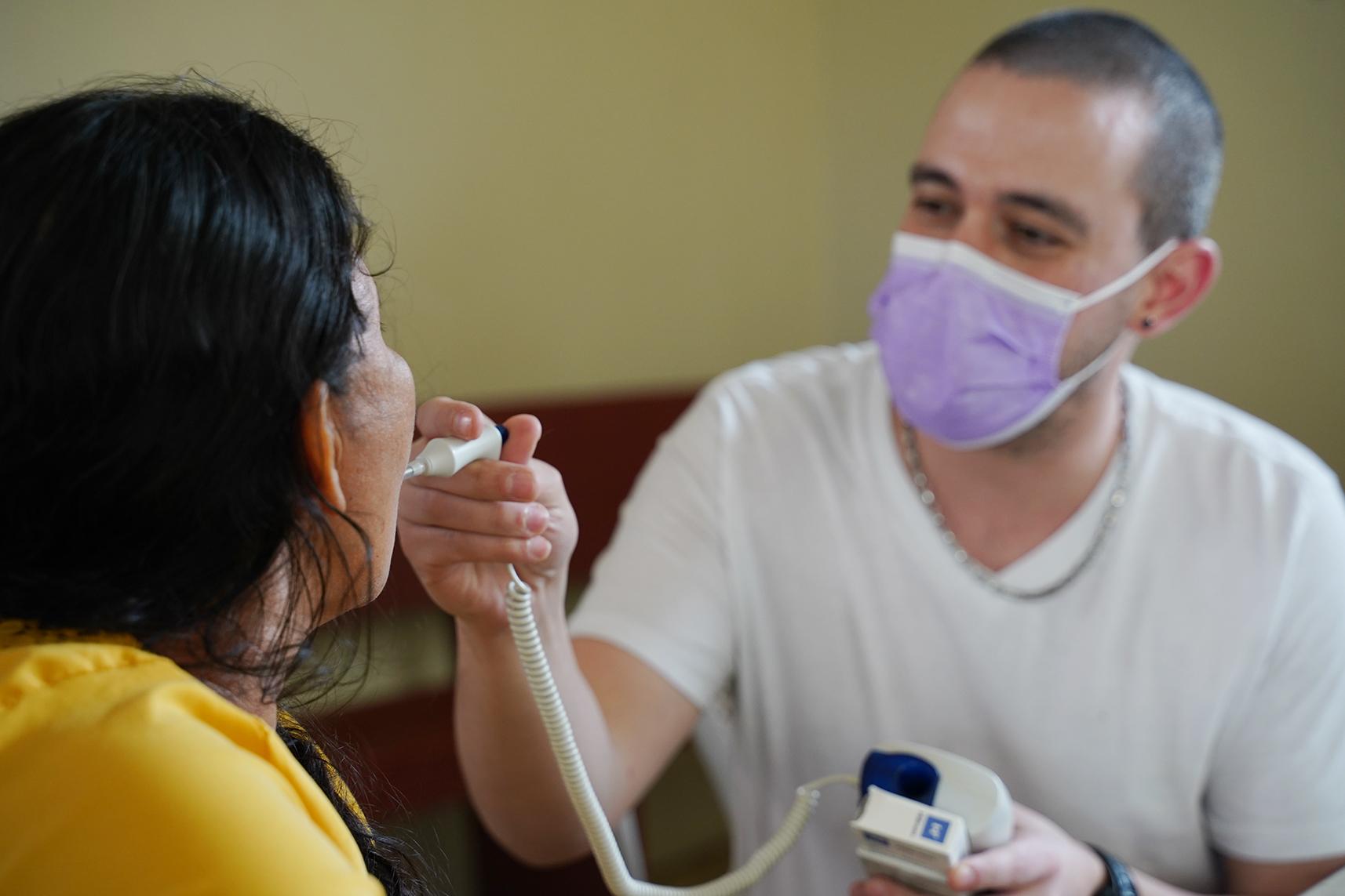 A person places a thermometer in another person’s mouth.