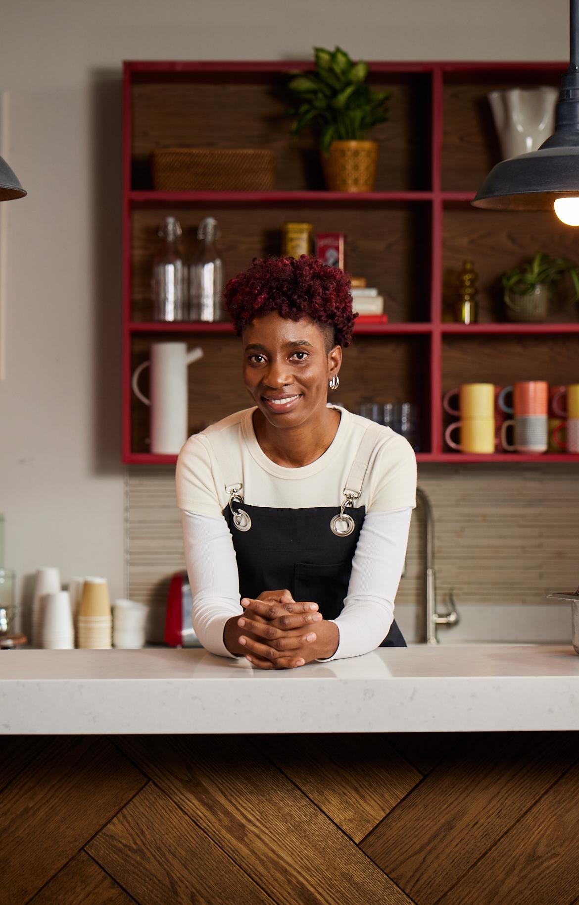 A smiling person rests their arms on a kitchen counter.