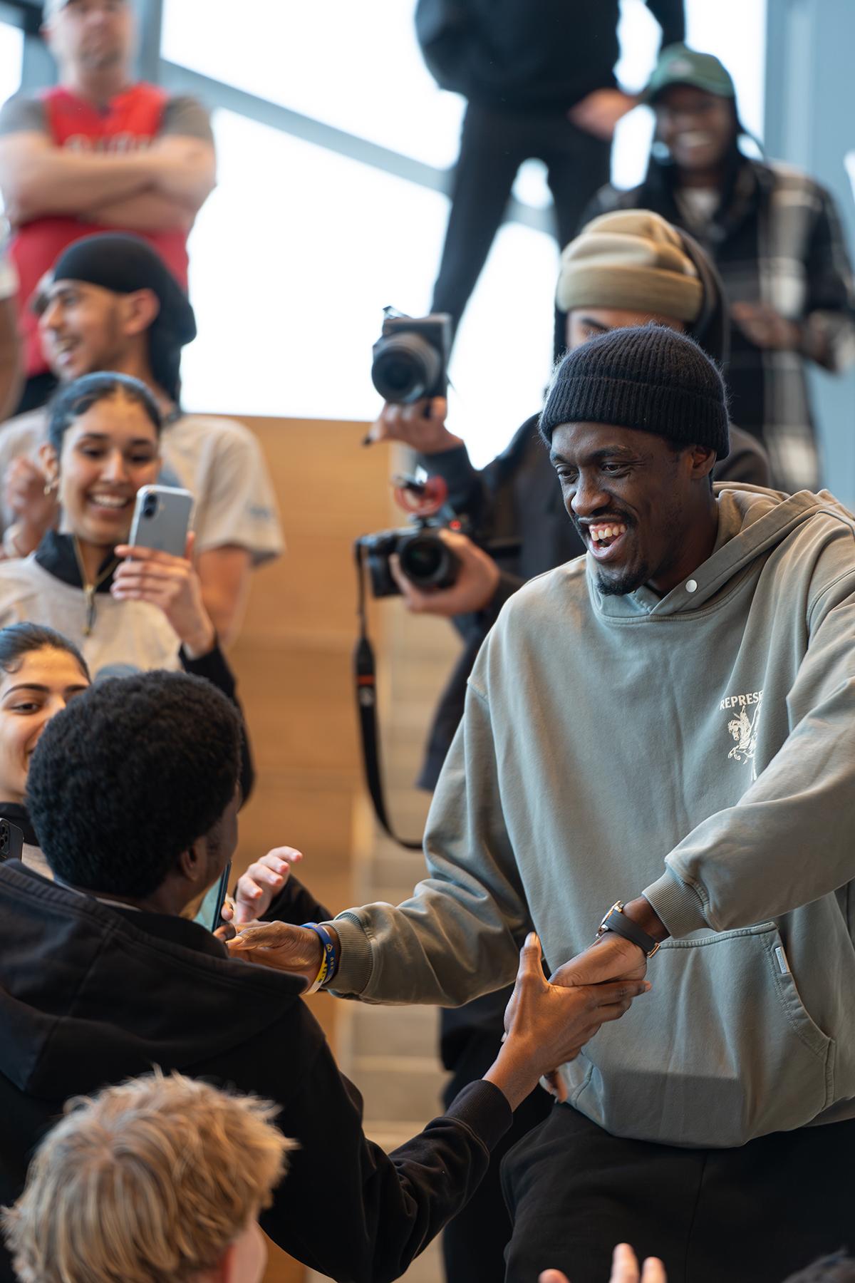 A person shakes hands with people as they walk down a flight of stairs.