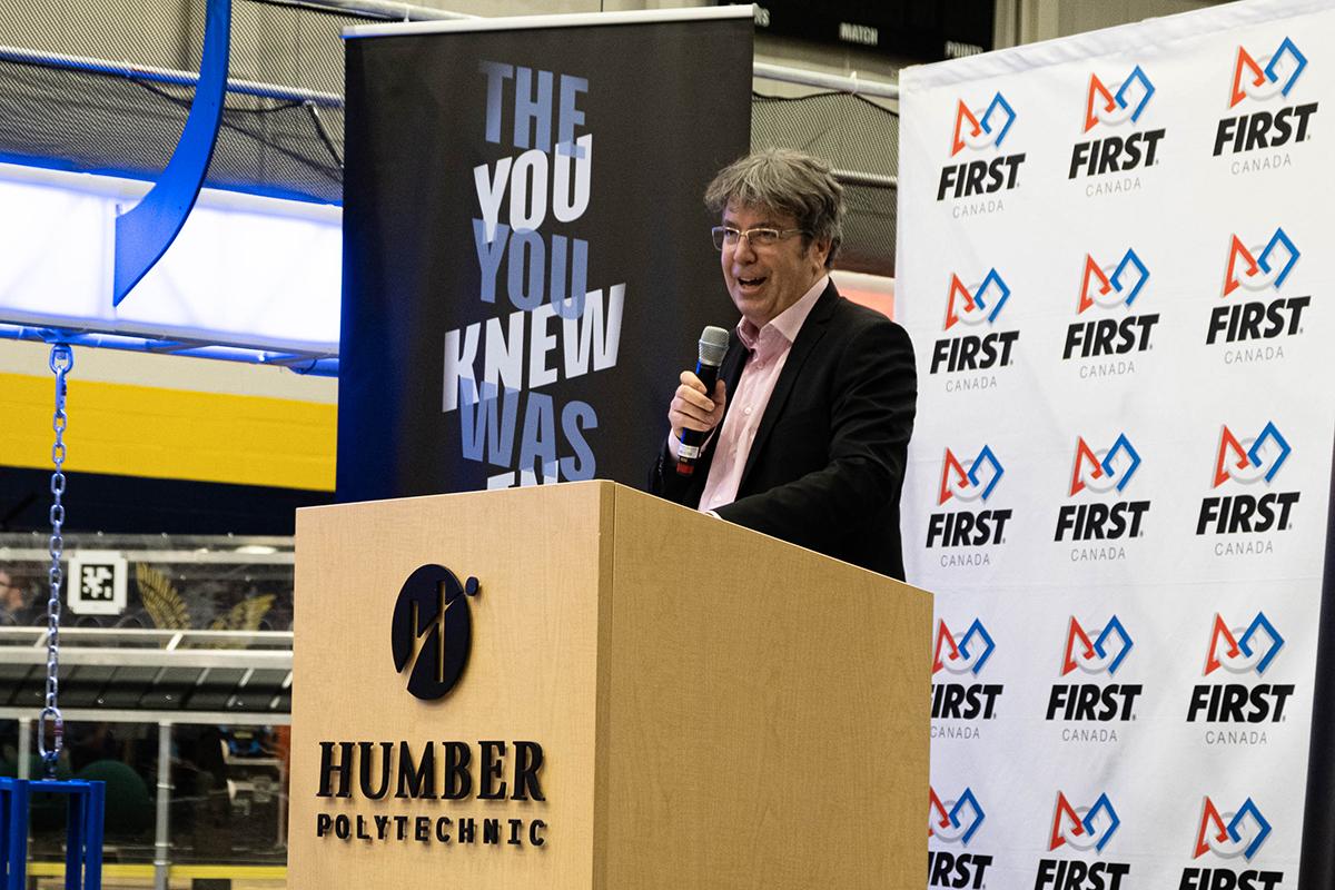 A person standing at a podium with the Humber Polytechnic logo on it speaks into a microphone.