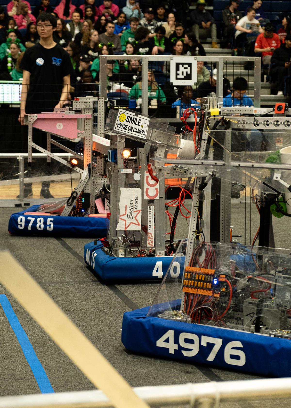 Several robots are lined up in a row as an audience watches.