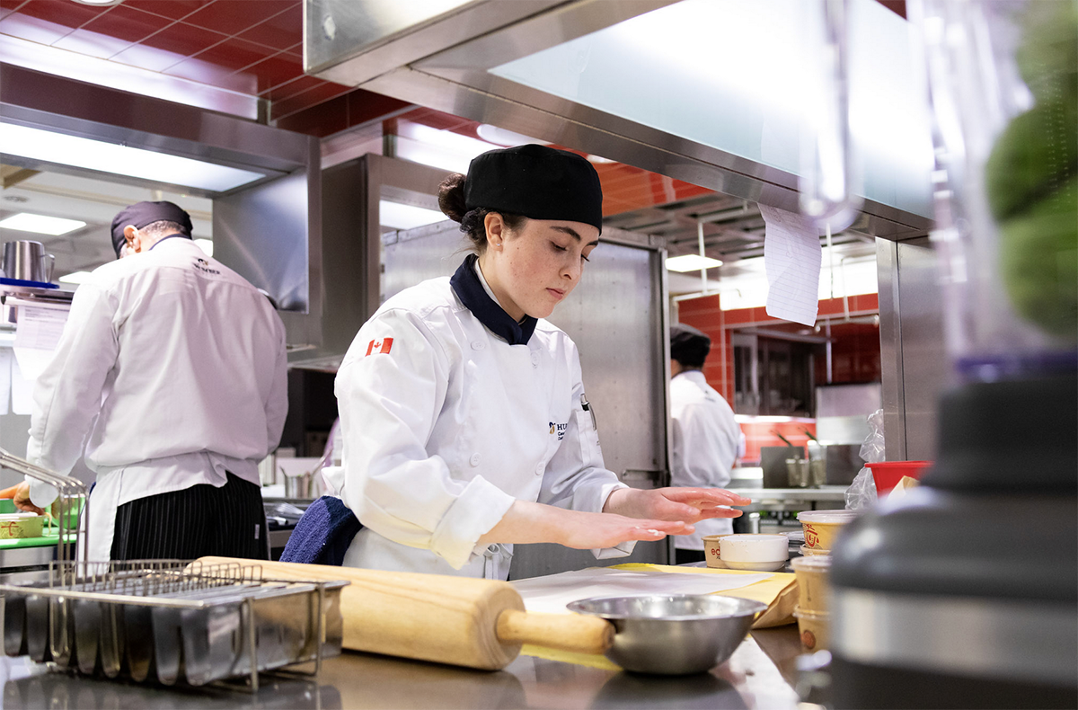 A person wearing a chef’s uniform cooks in a kitchen.