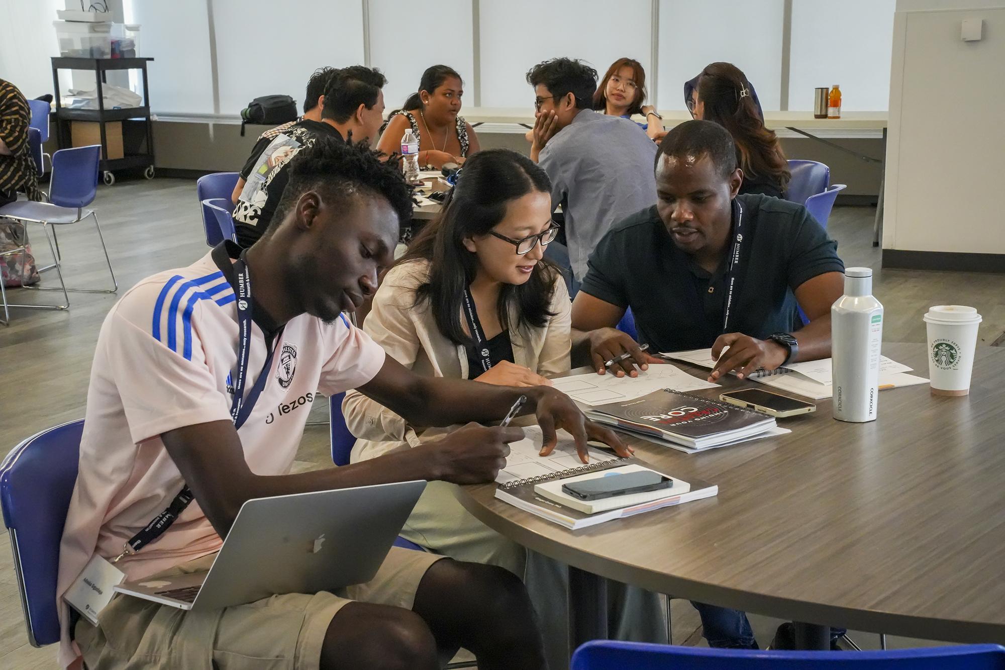 Three people sitting around a table have a discussion while looking at documents and textbooks.