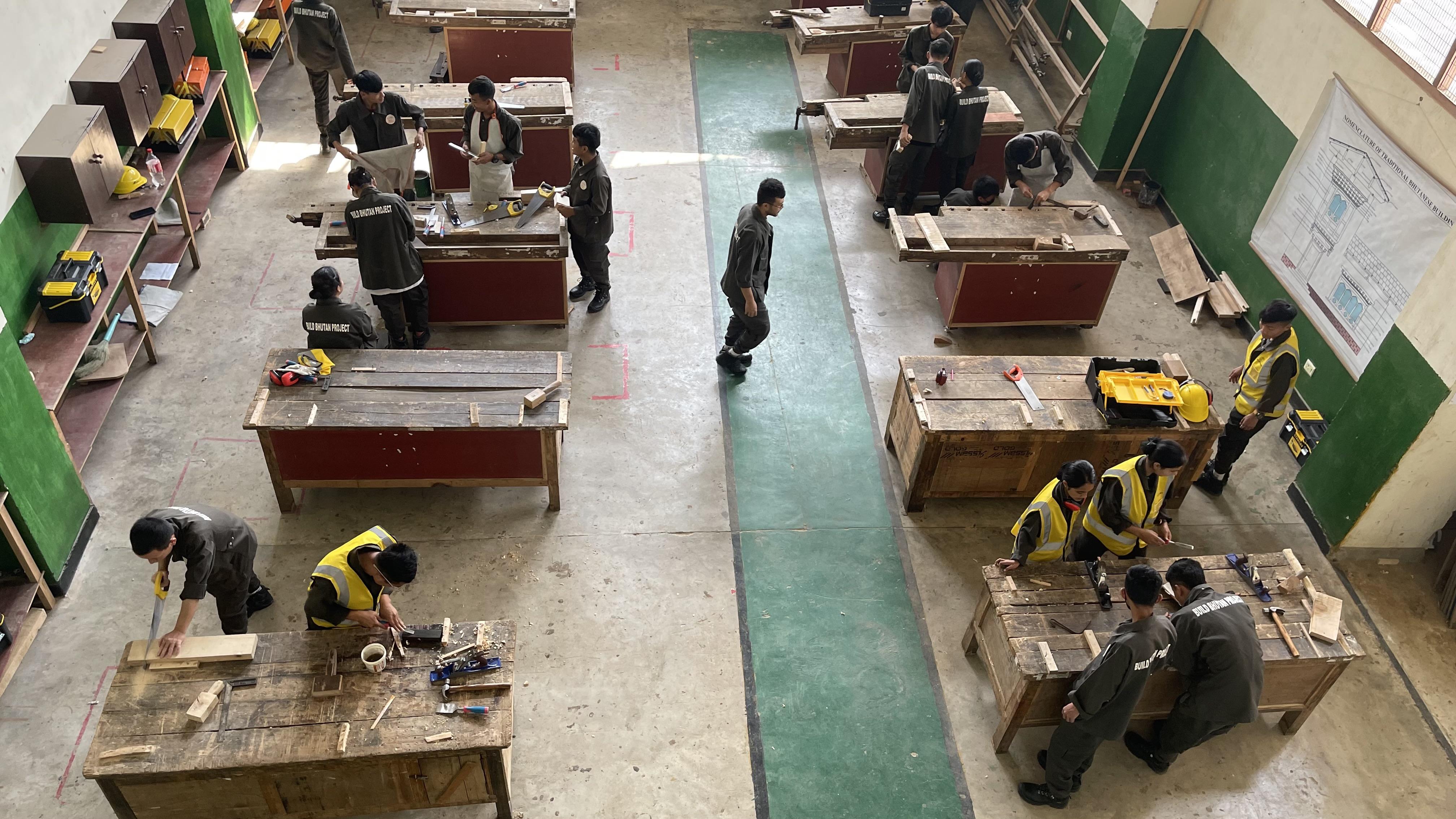 A series of tables in a room with tools and materials on them. People are working at the tables on projects.