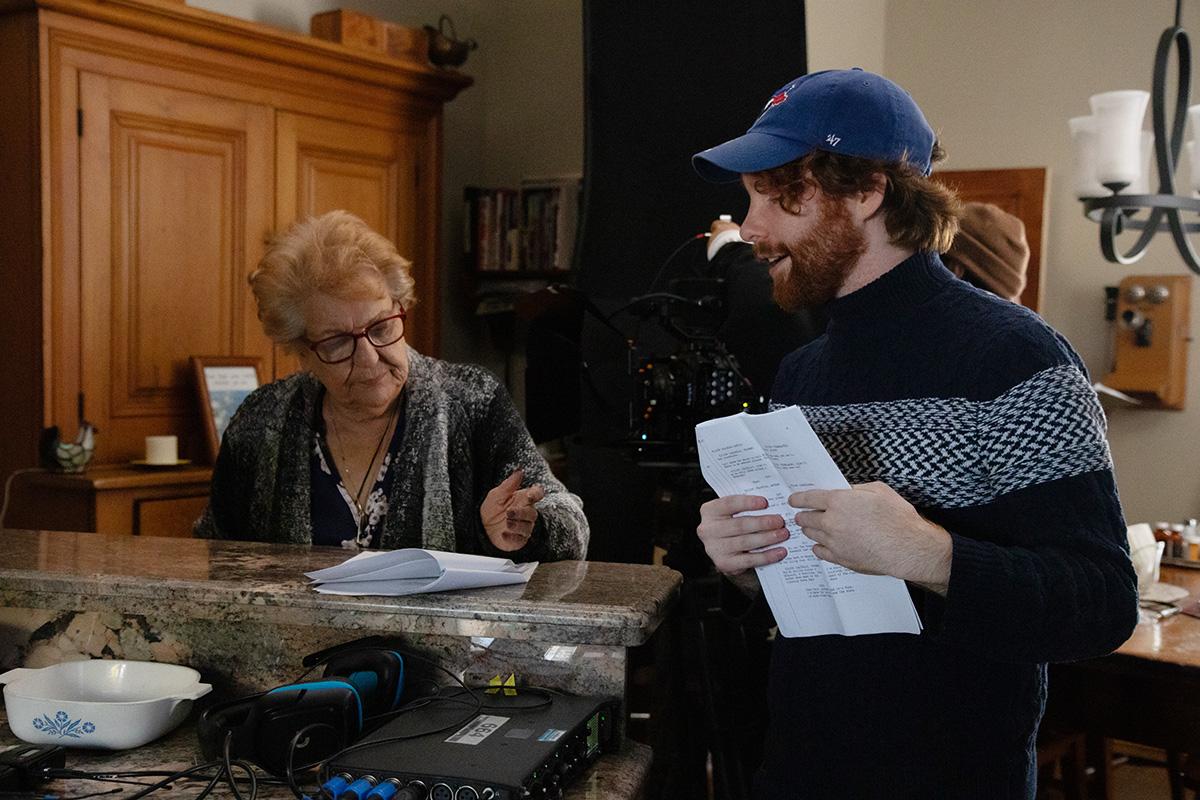 A person speaks to another person on a film set. Both are looking at scripts.