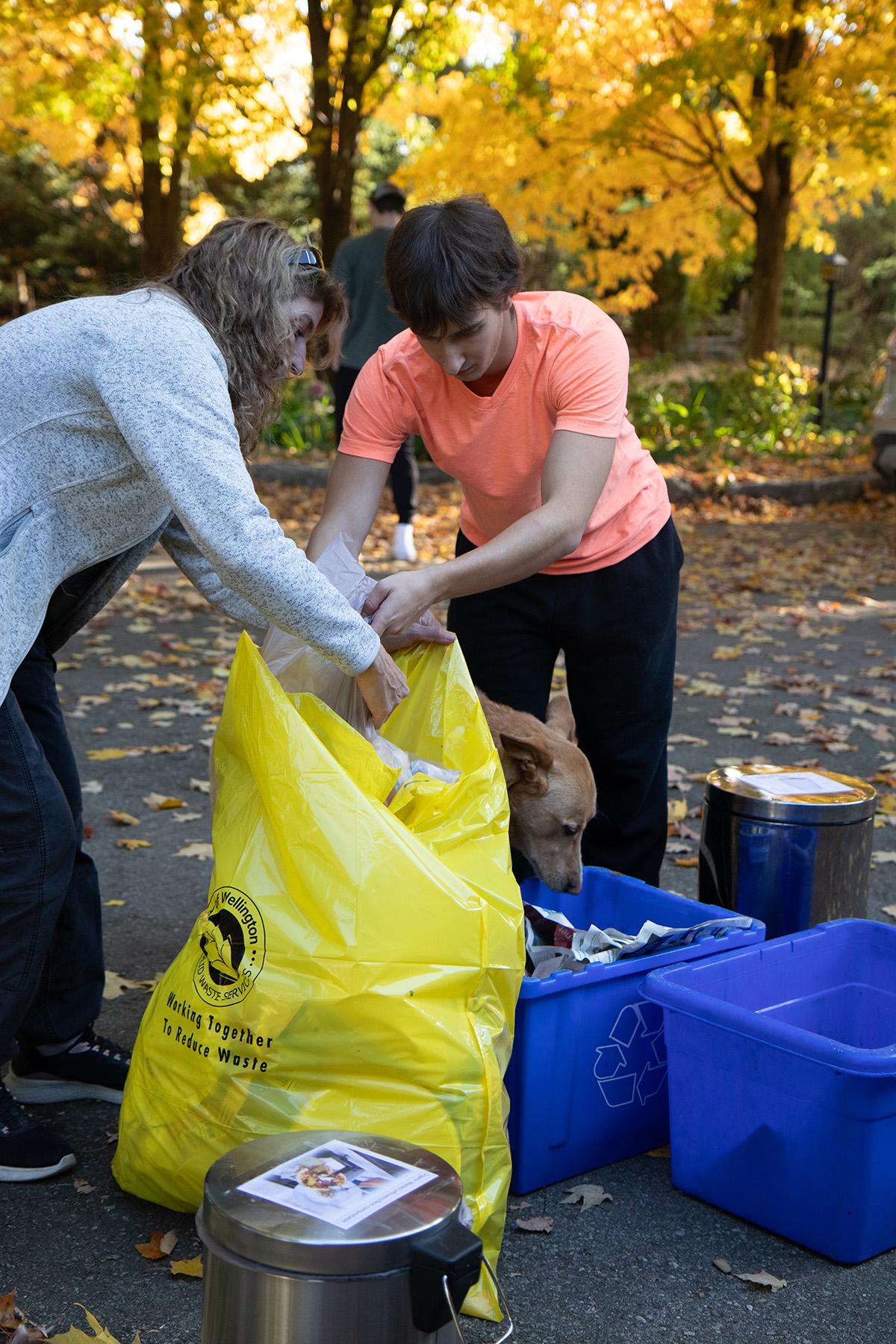 Two people are sorting recyclables and placing them in a large yellow bag.