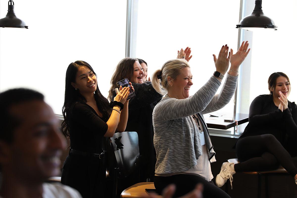 Smiling people are standing and clapping.