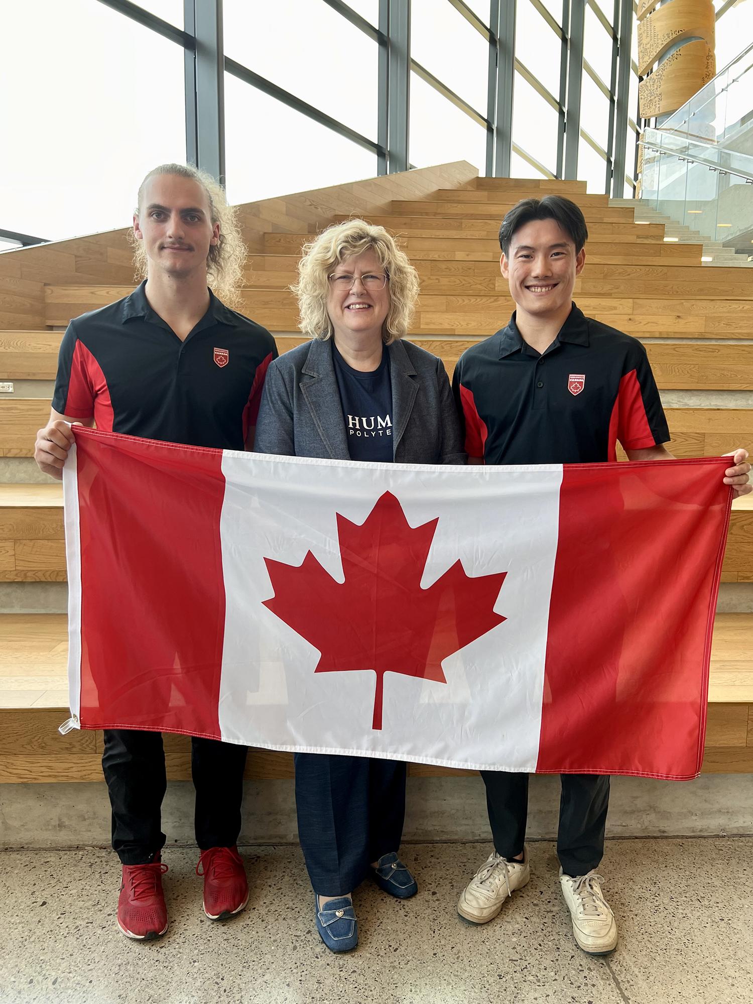 Three smiling people stand together holding the Canadian flag.