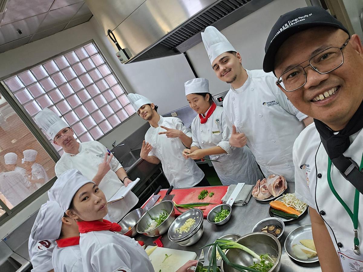 A group of people wearing chef’s outfits are in a kitchen.