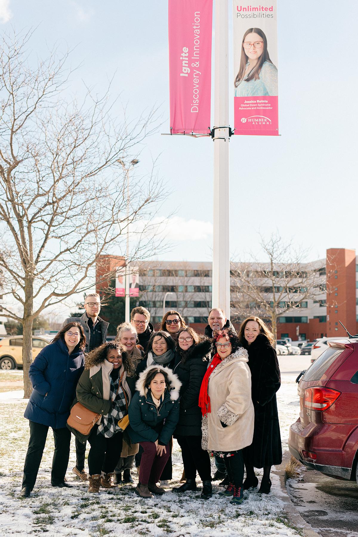 A group of people stand outside beneath a banner with the image of a person on it.