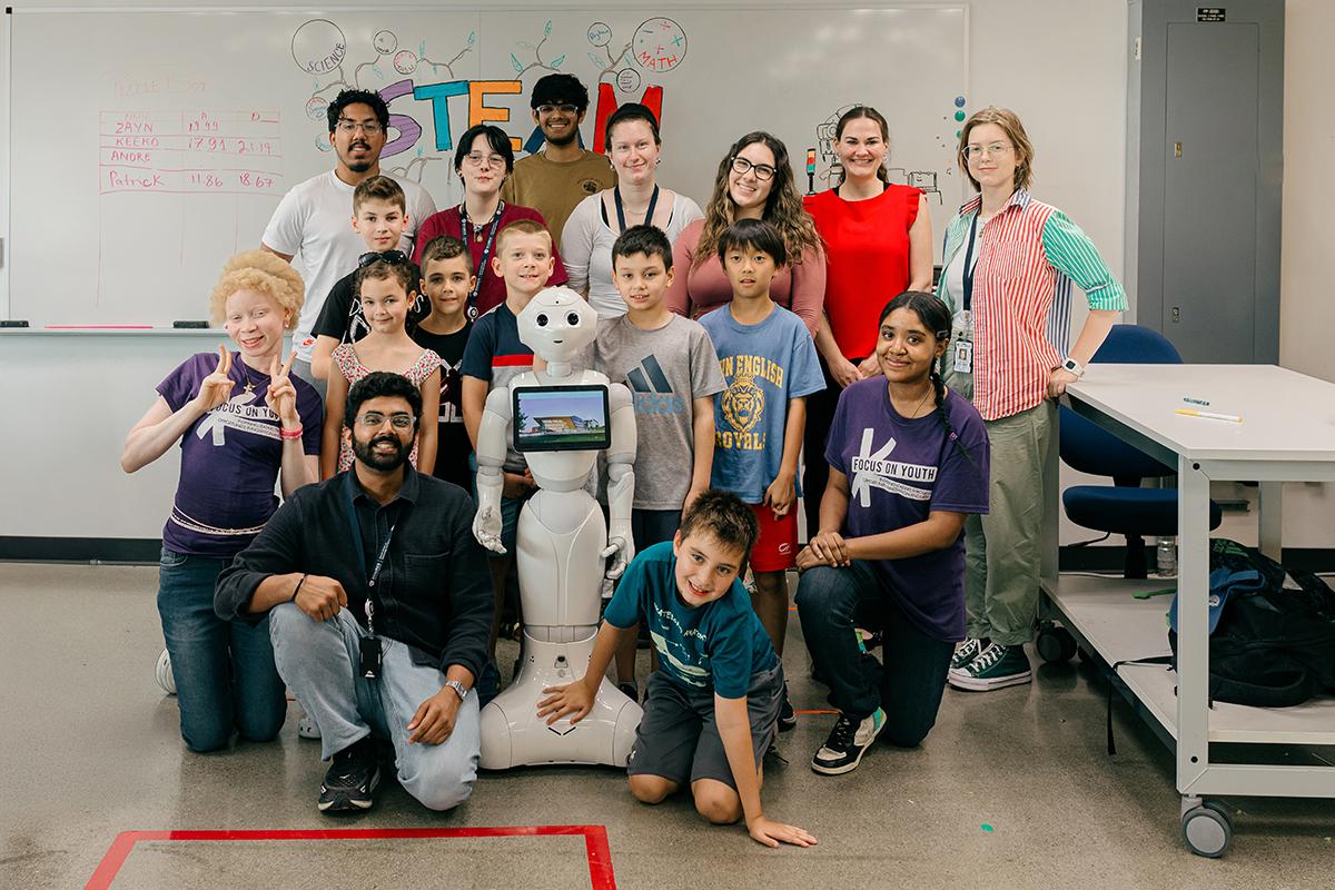 A group of youth stand together around a robot in a lab.