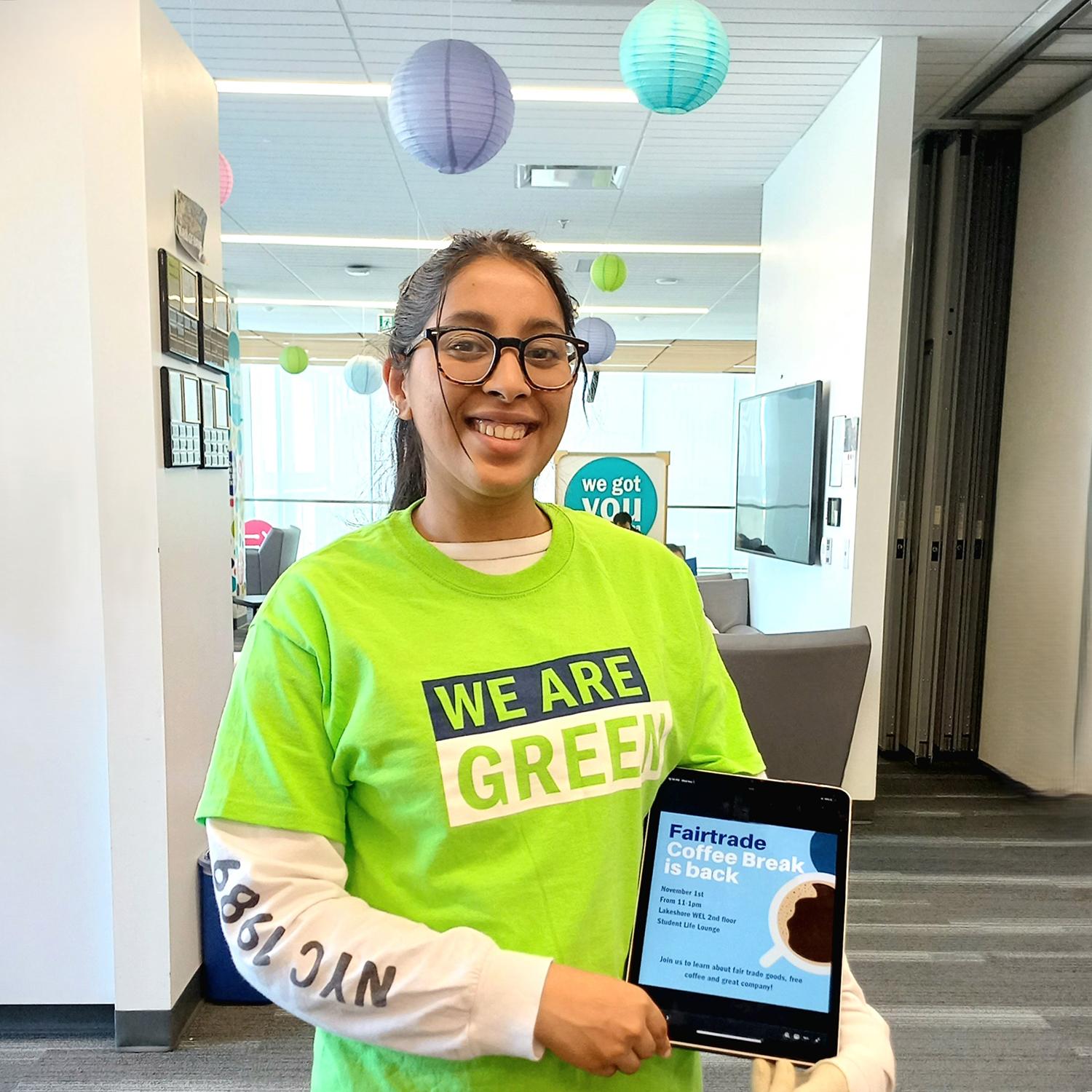 A person holds a tablet while wearing a shirt that reads We Are Green.