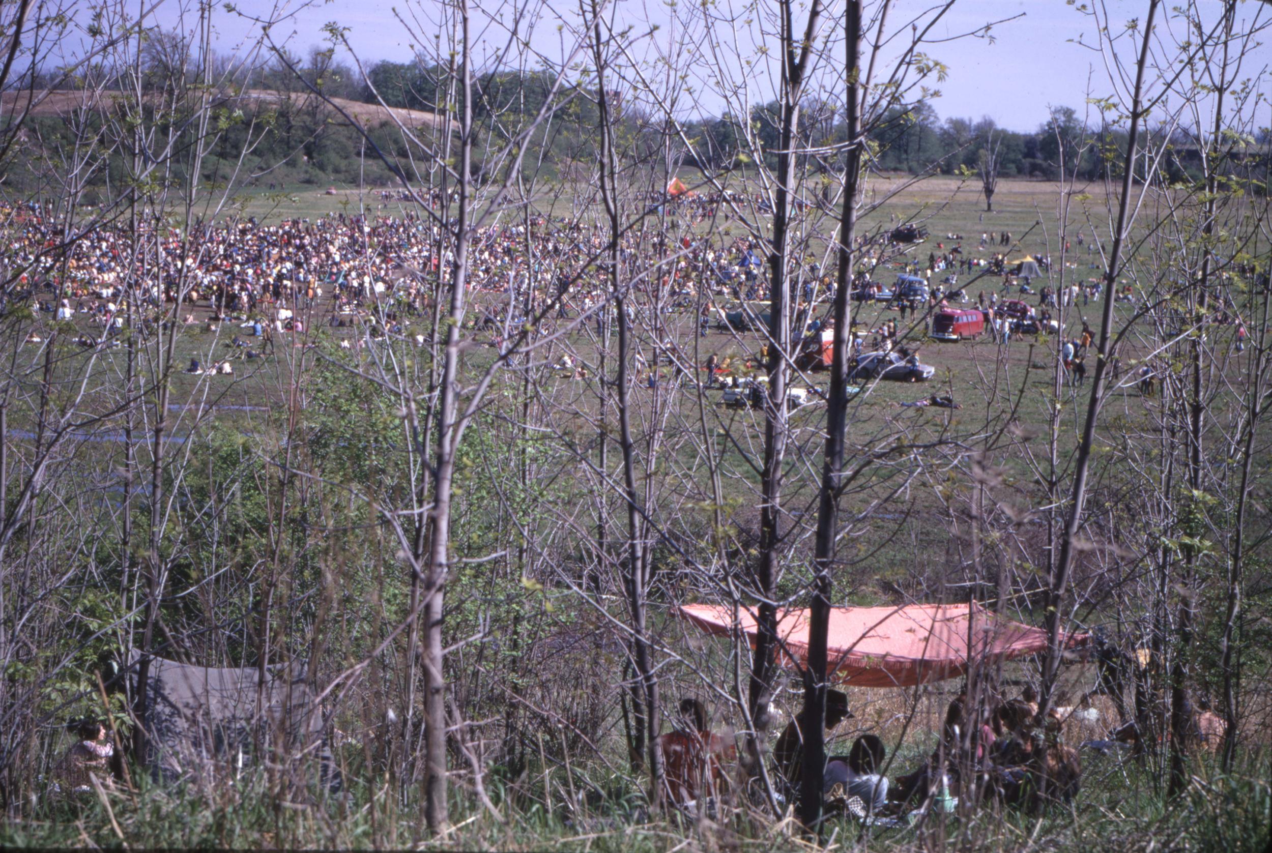 A field filled with people as well as tents and vehicles.