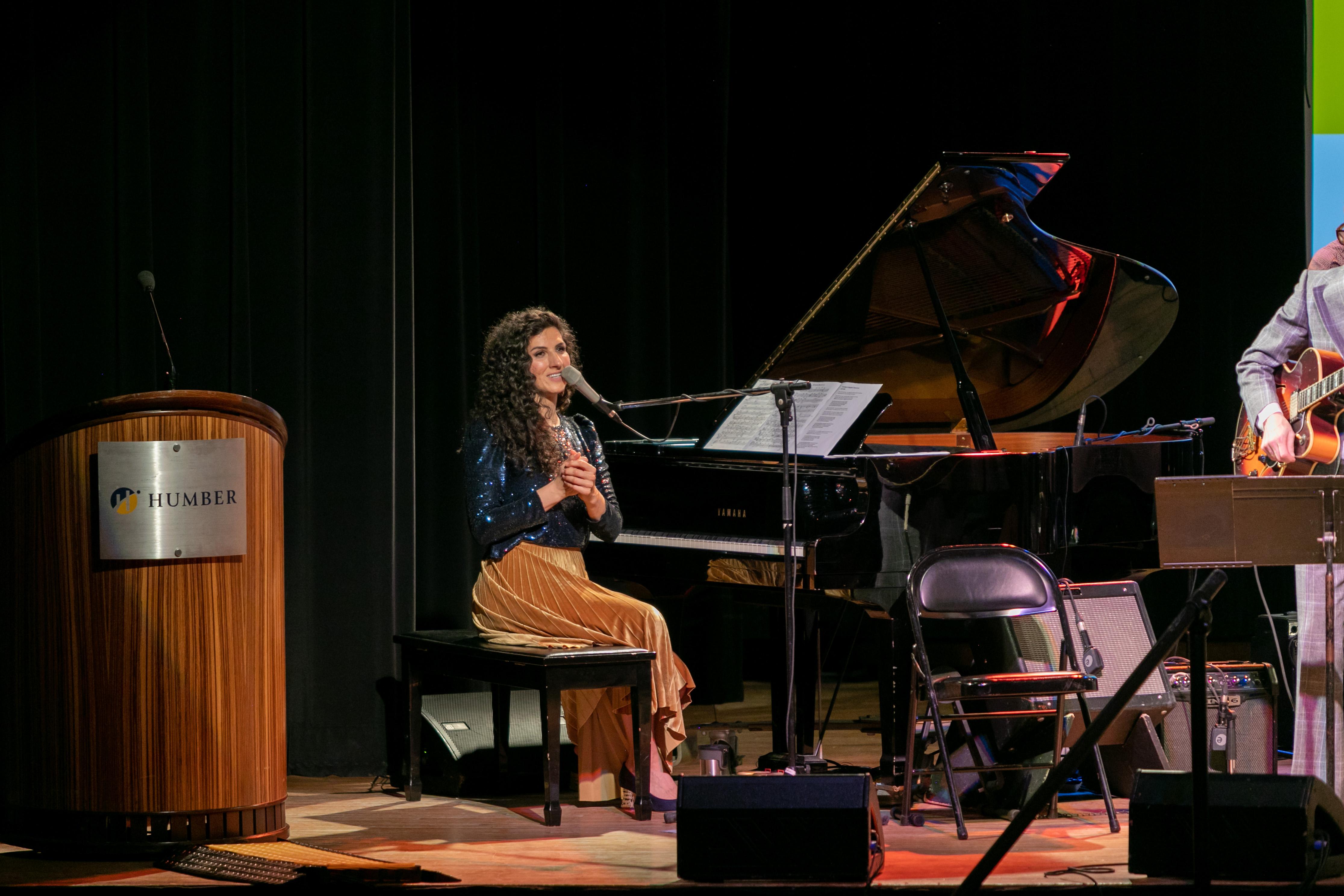 A person sits at a piano while speaking into a microphone.