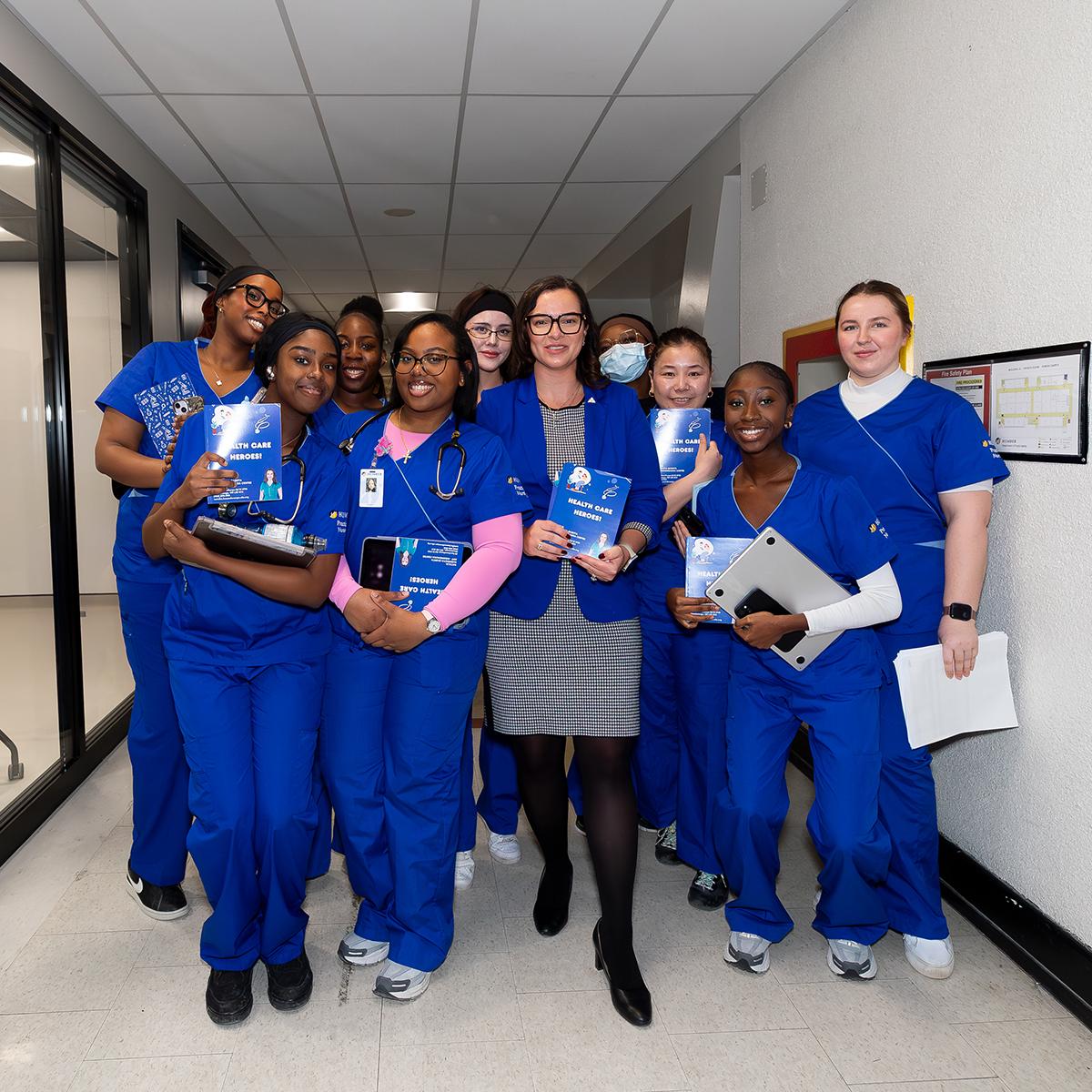 A person holding a book stands among a group of students wearing medical scrubs.