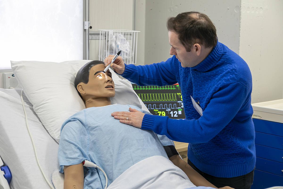 The Living Classroom at The Village of Humber Heights is a partnership between Humber’s Faculty of Health & Life Sciences and Schlegel Villages. A person is using a light to look at the eyes of a training dummy.