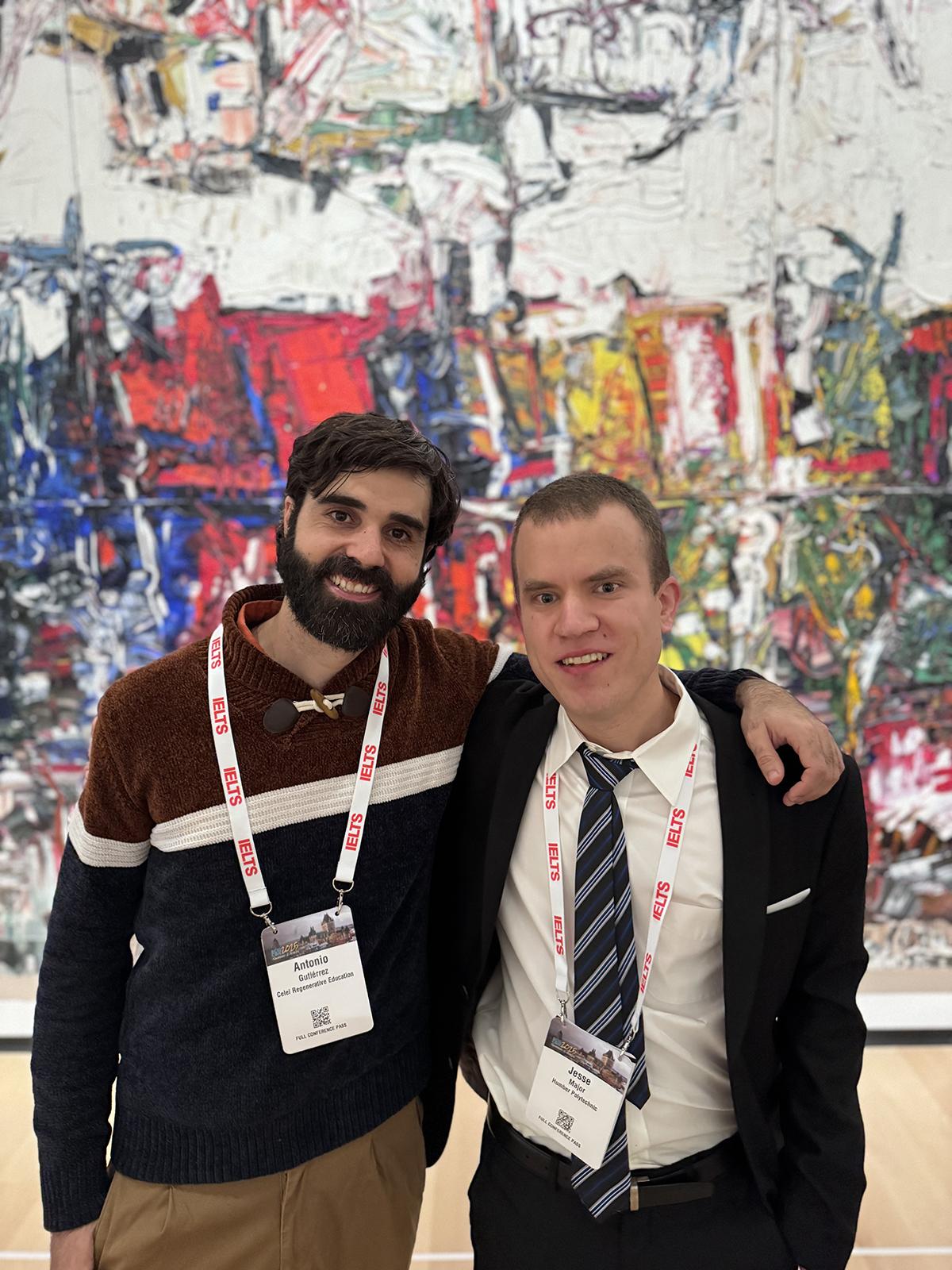 Two people are standing together with their arms around each other’s shoulders.