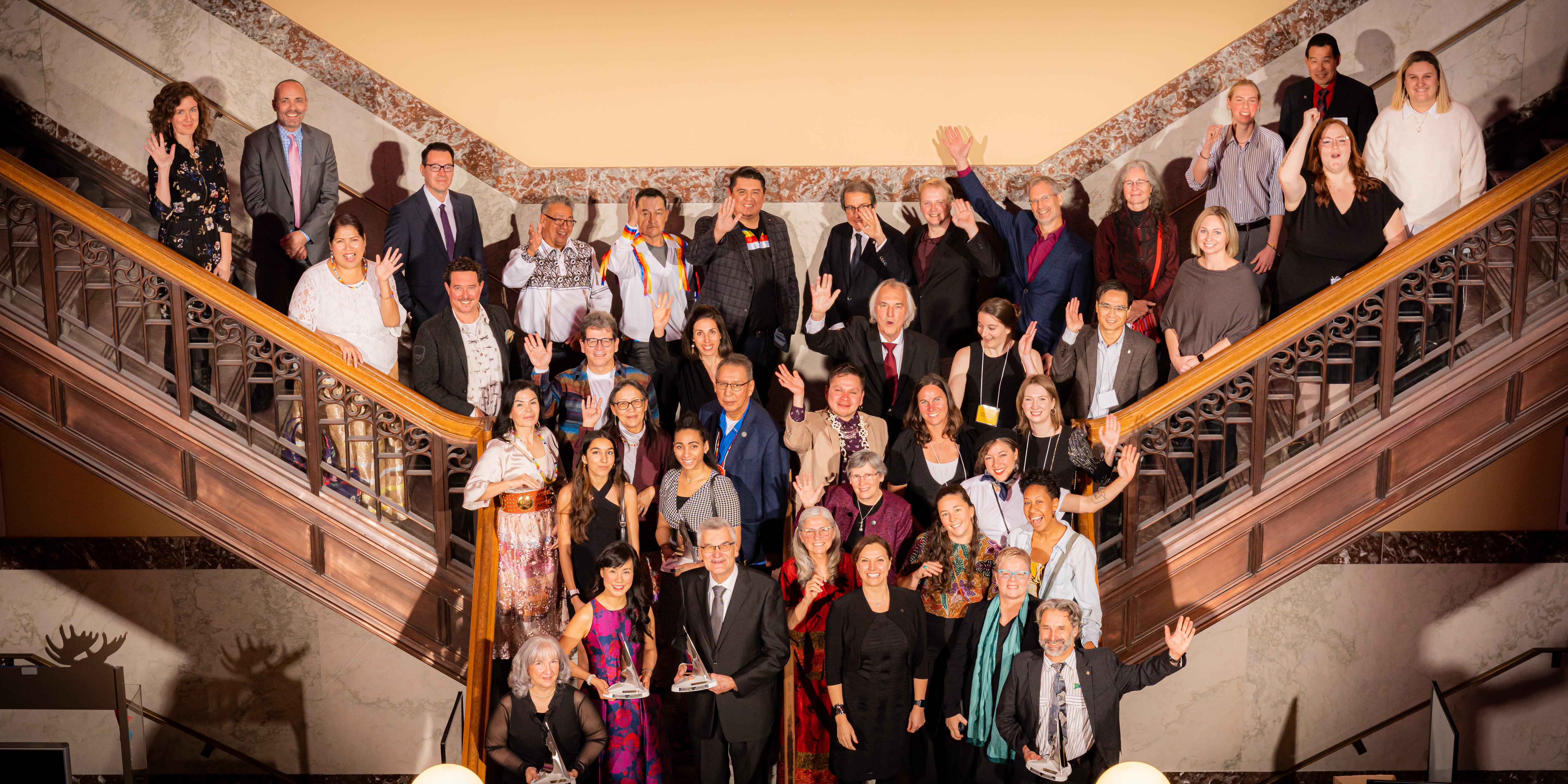 The finalists and winners from the Nature Inspiration awards stand on a staircase and wave. 