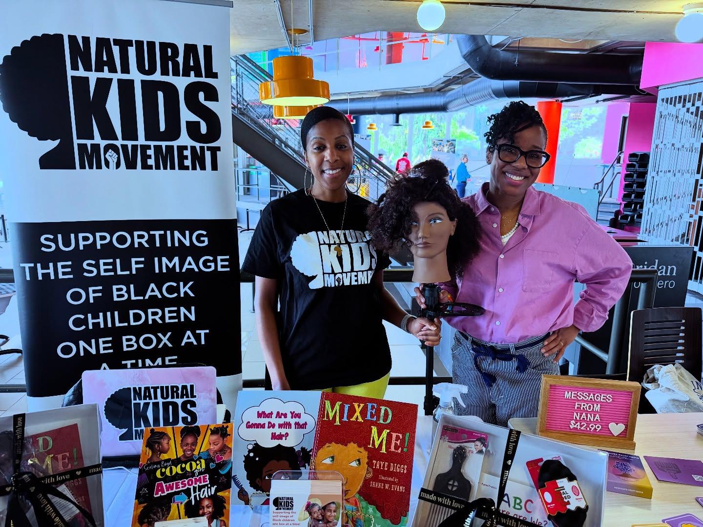 Two smiling people are standing next to a banner that reads Natural Kids Movement.