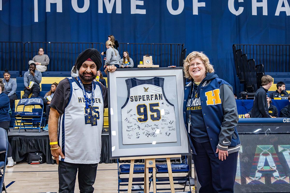 Two people stand next to a framed Humber Hawks jersey.