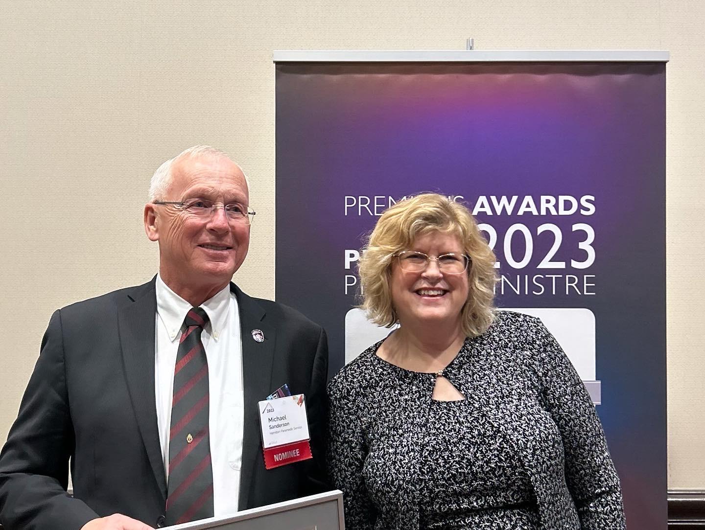 Two smiling people stand in front of a banner that reads Premier’s Awards 2023.