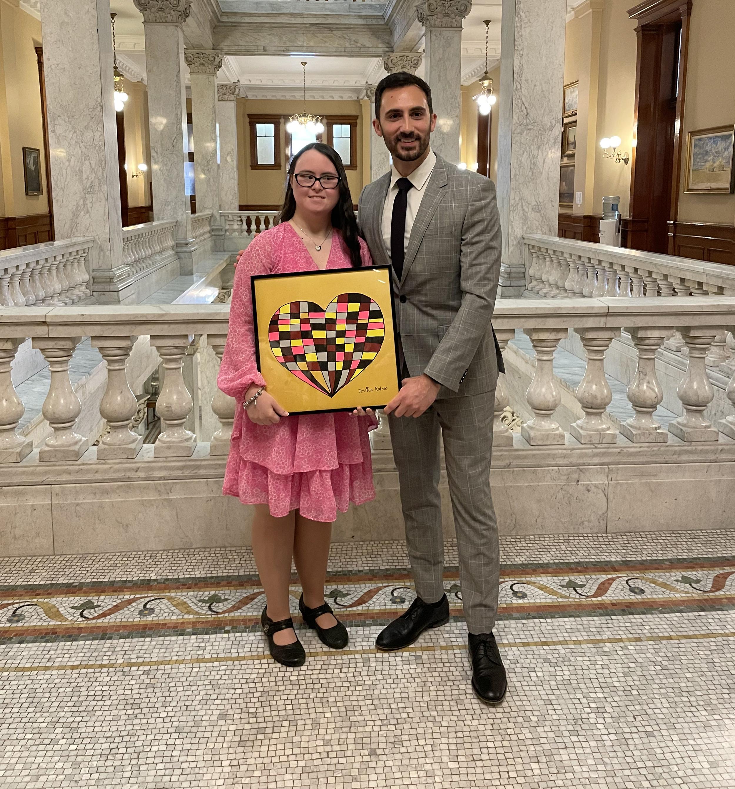 Two people pose for a photo holding a painting of a heart.