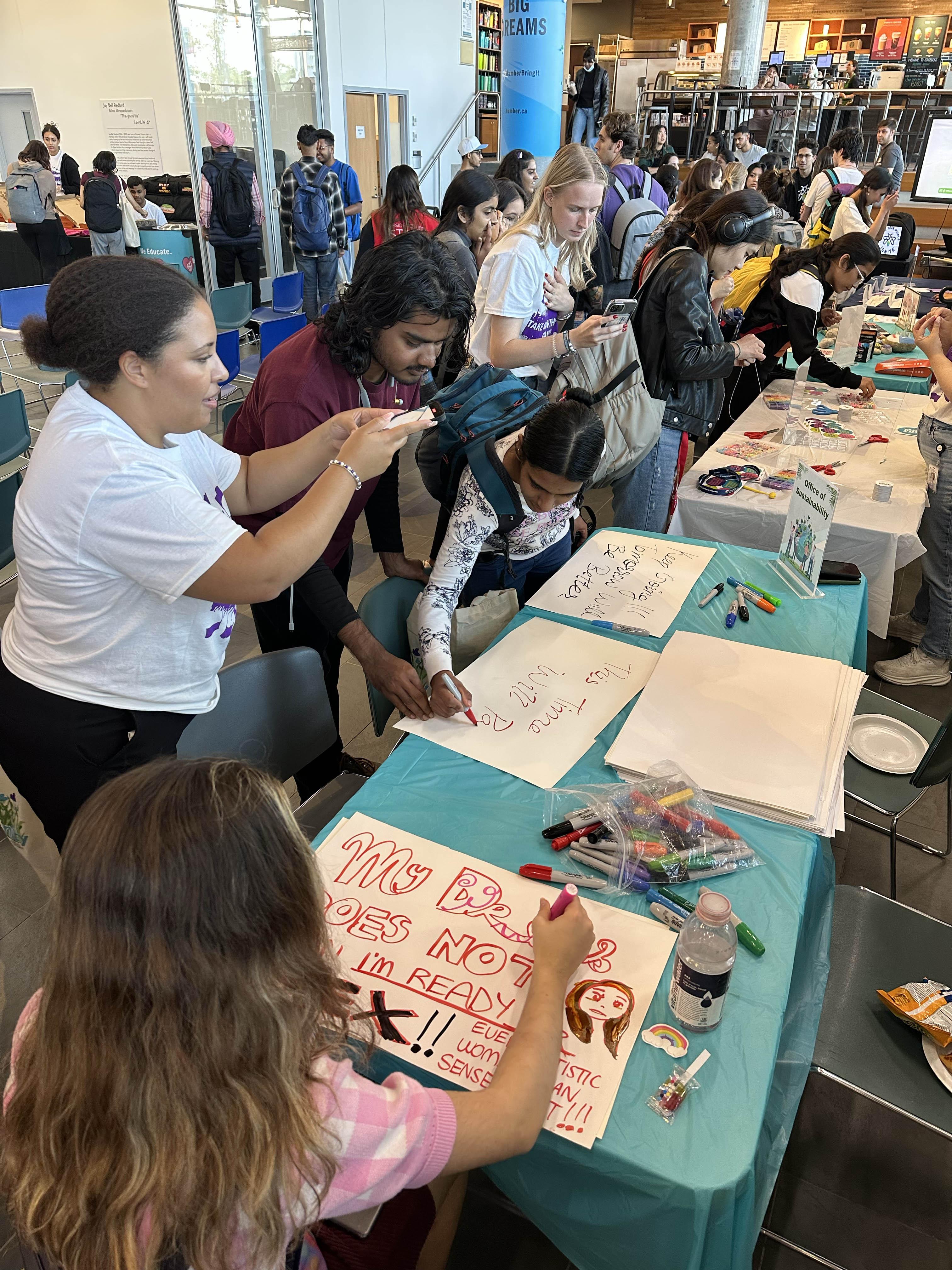 People sitting around a table use markers to create signs to carry with them as they take part in Take Back the Night at Humber 
