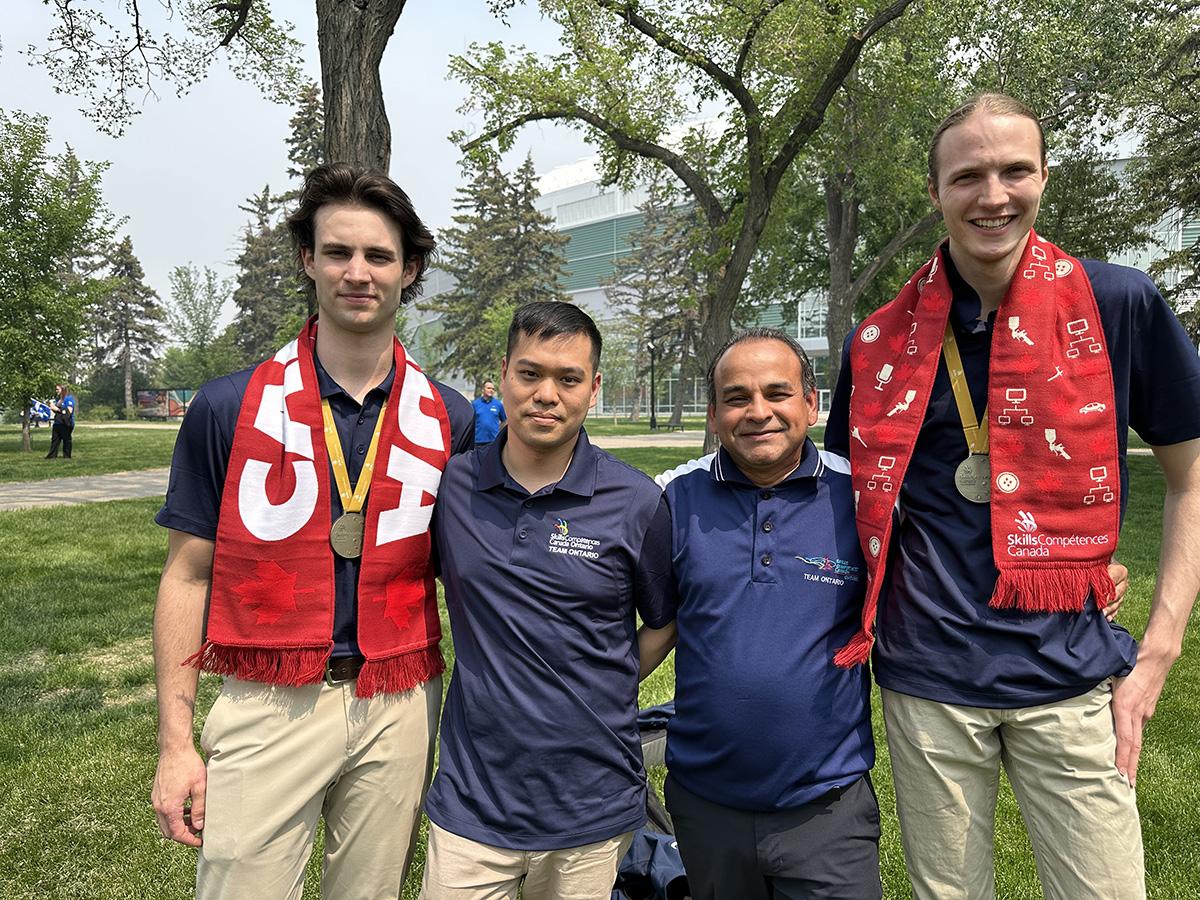 Four people stand arm-in-arm and two of them are wearing gold medals around their necks.