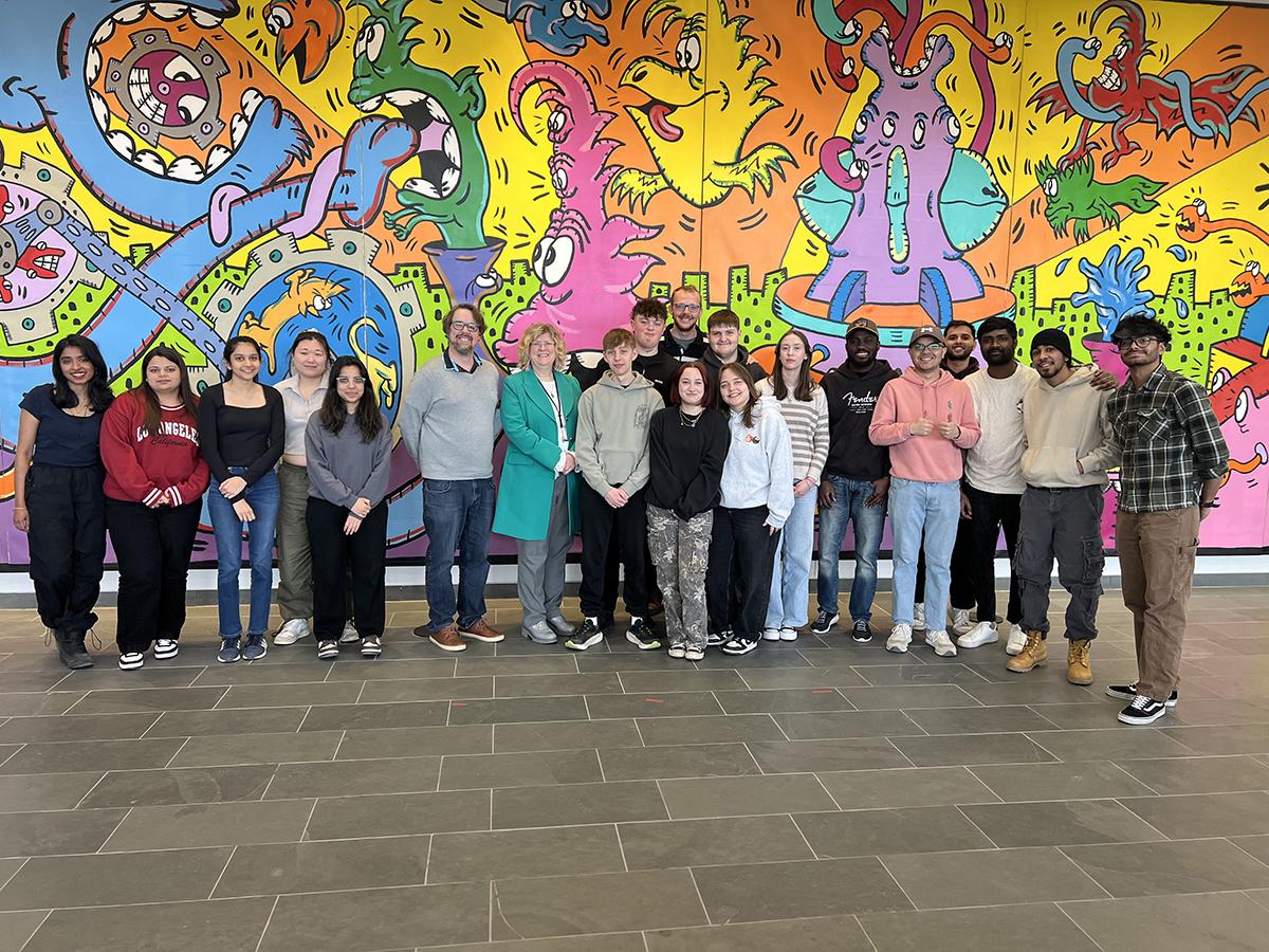 A group of people stand in front of a colourful mural.