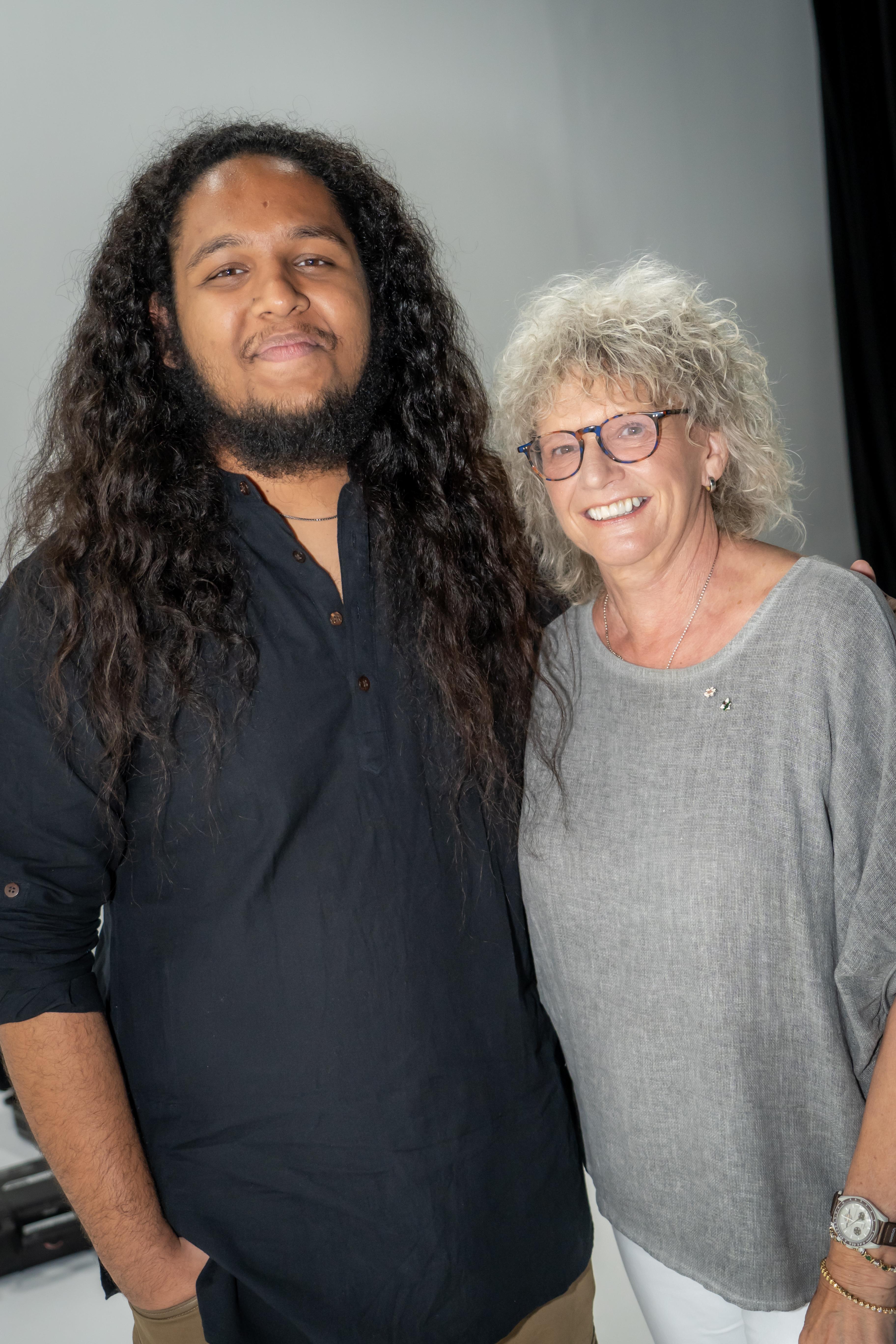 Two smiling people stand together in front of a grey backdrop.