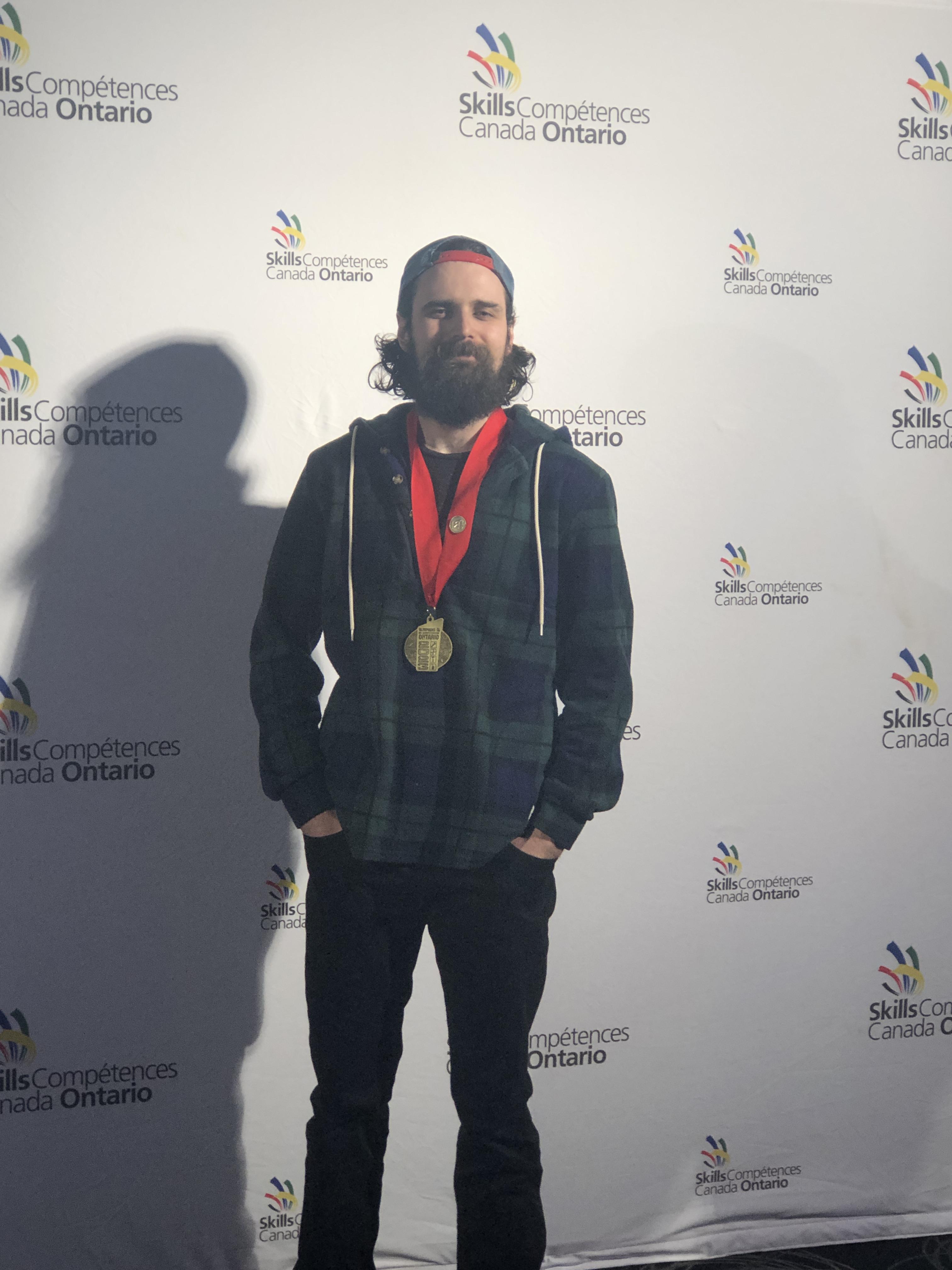 A person smiles and poses for a photo while wearing a gold medal around their neck.