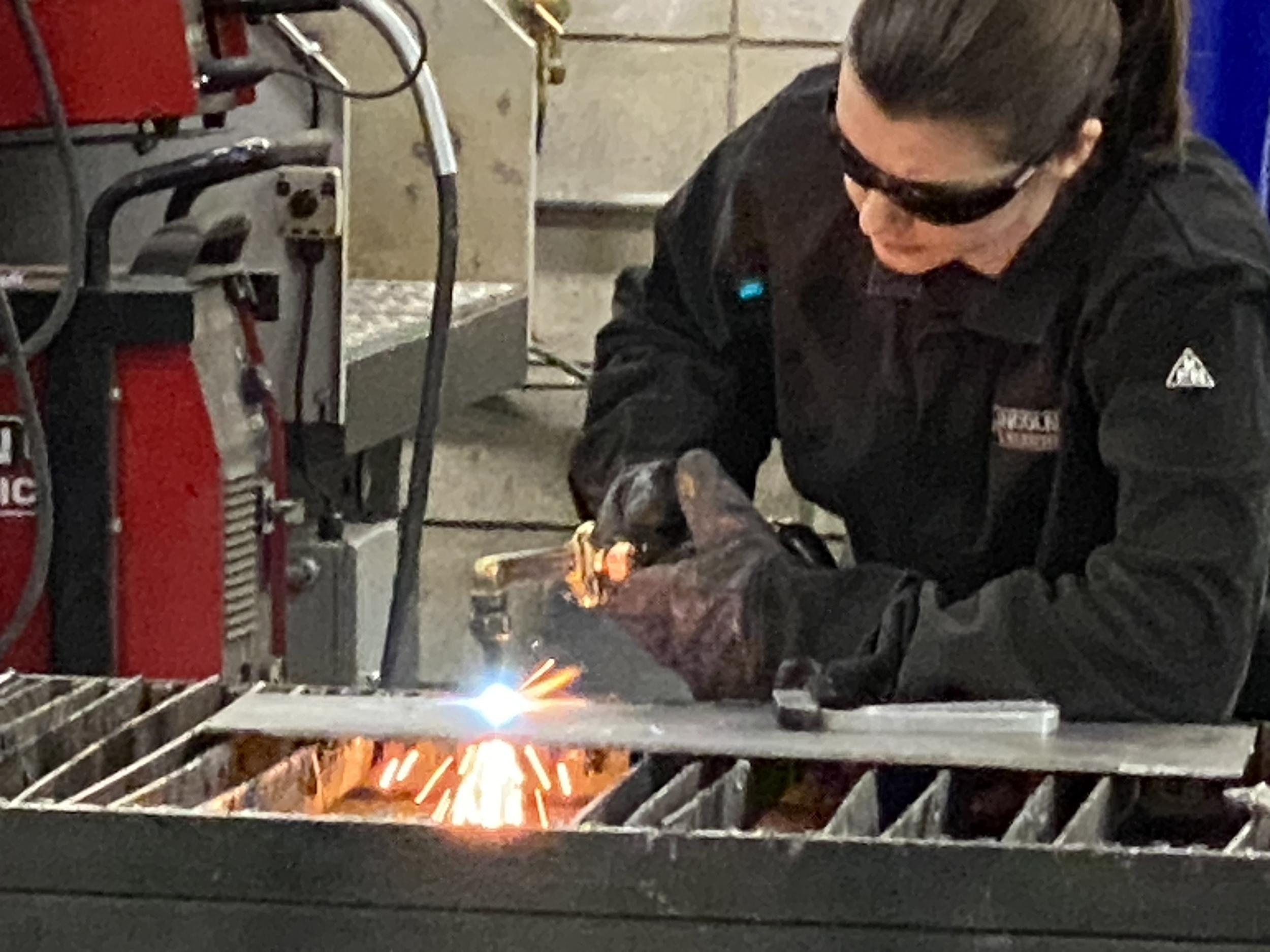 A person wearing safety goggles and gloves uses a torch to weld metal.
