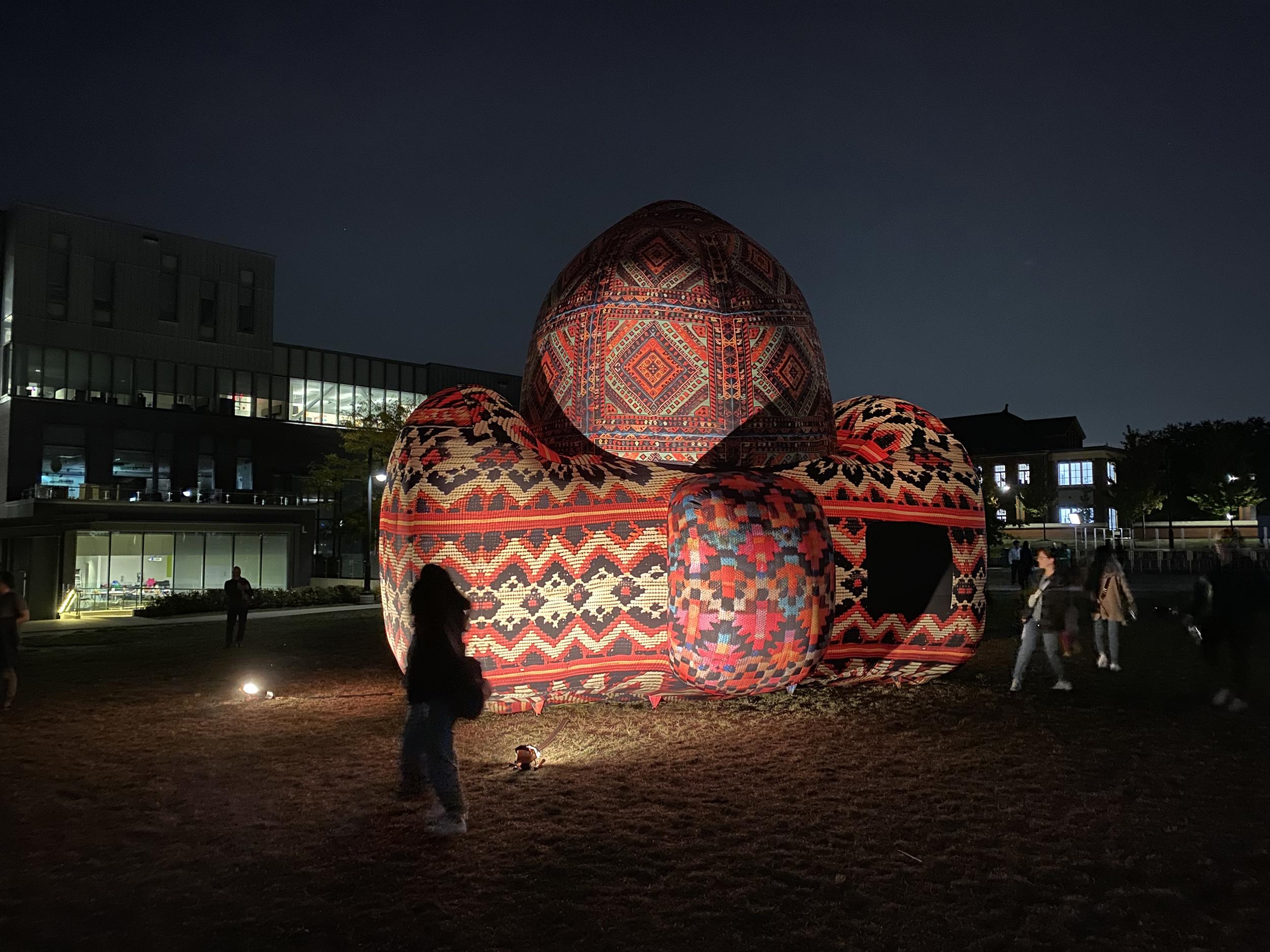 People walk past what appears to be an inflatable art project that’s lit up with lights.