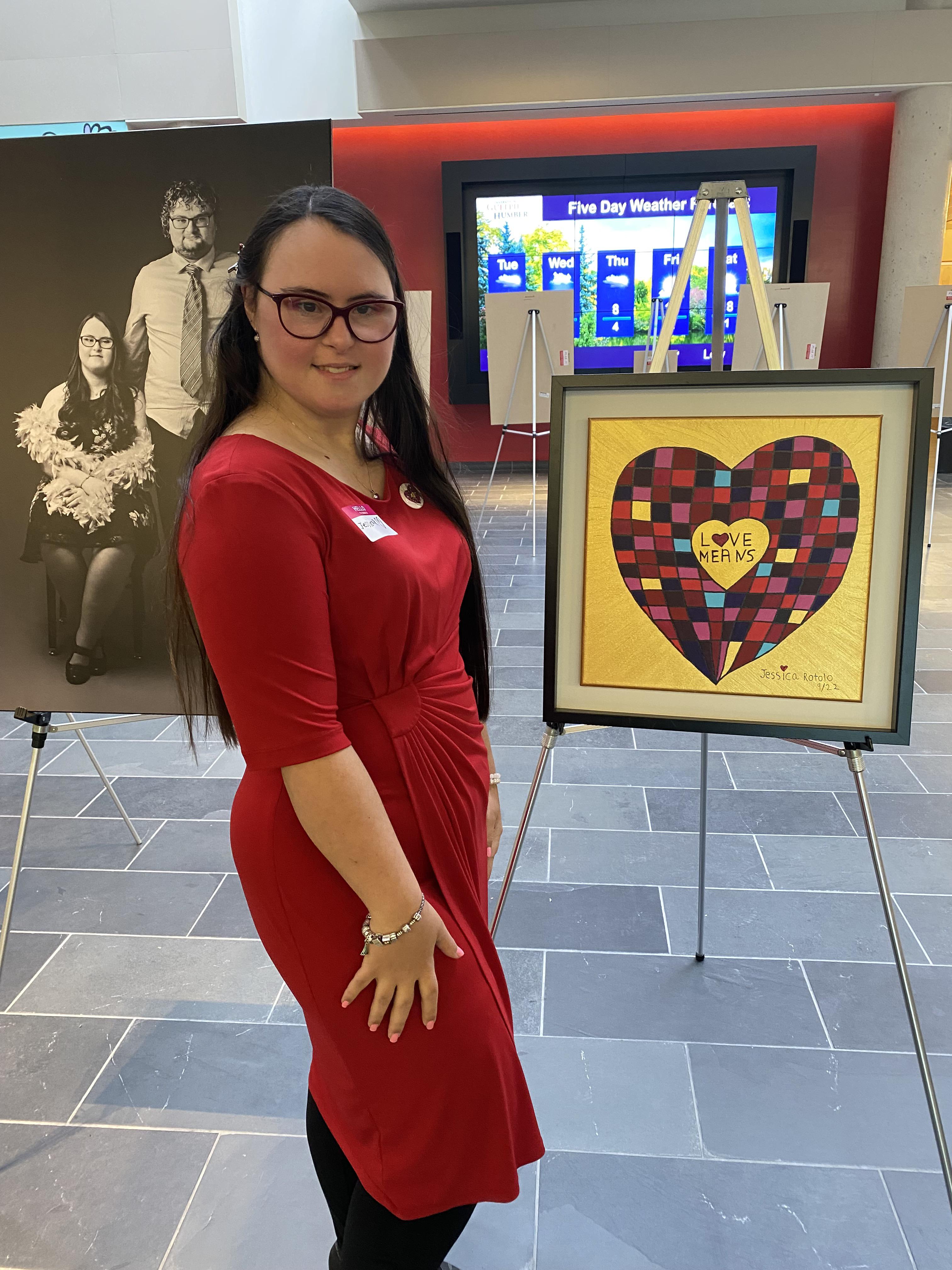 Jessica Rotolo stands next to her painting Love Means. A black and white photo of Jessica and her friends is in the background.