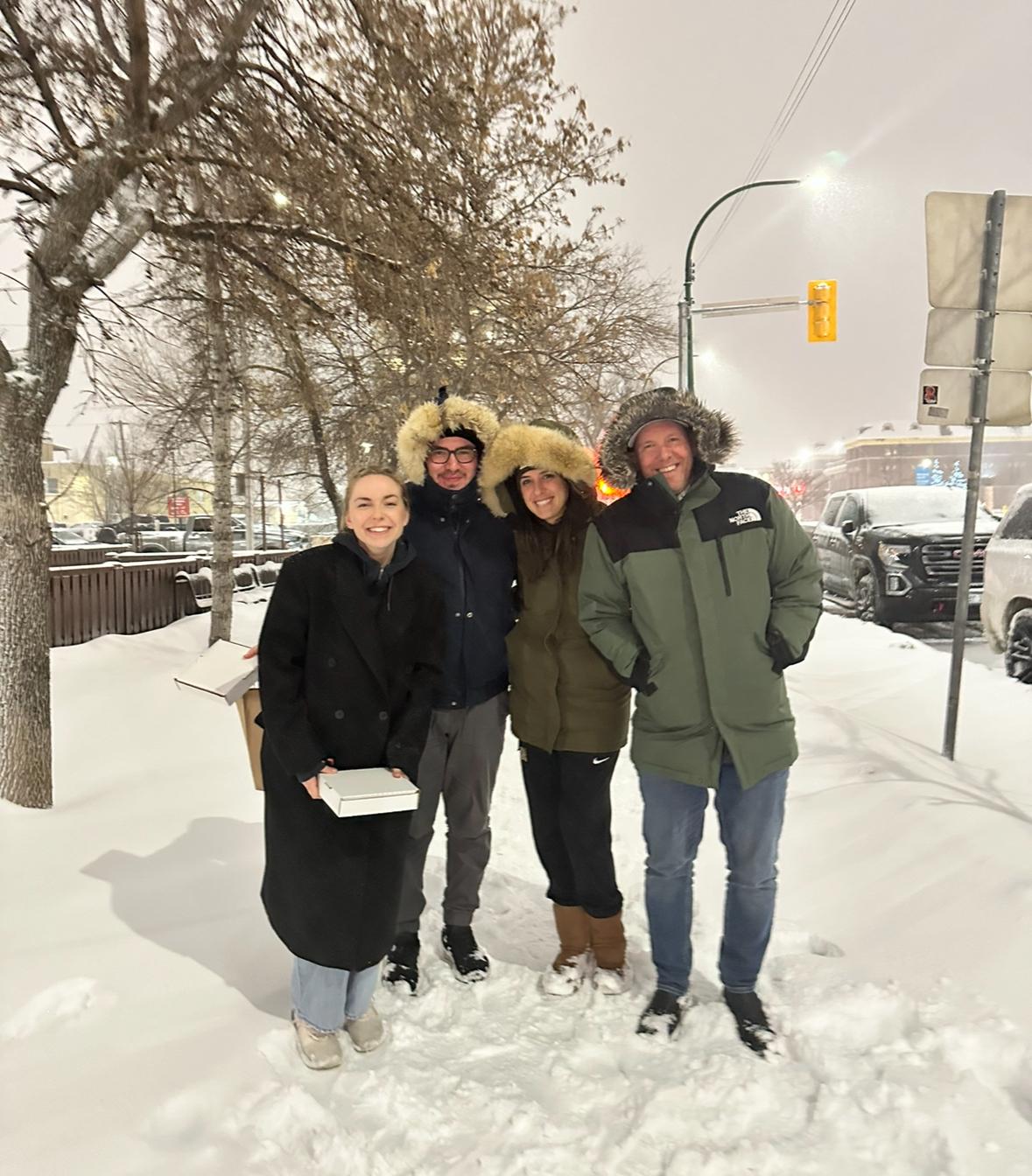 Four people wearing winter coats stand outside in the snow.