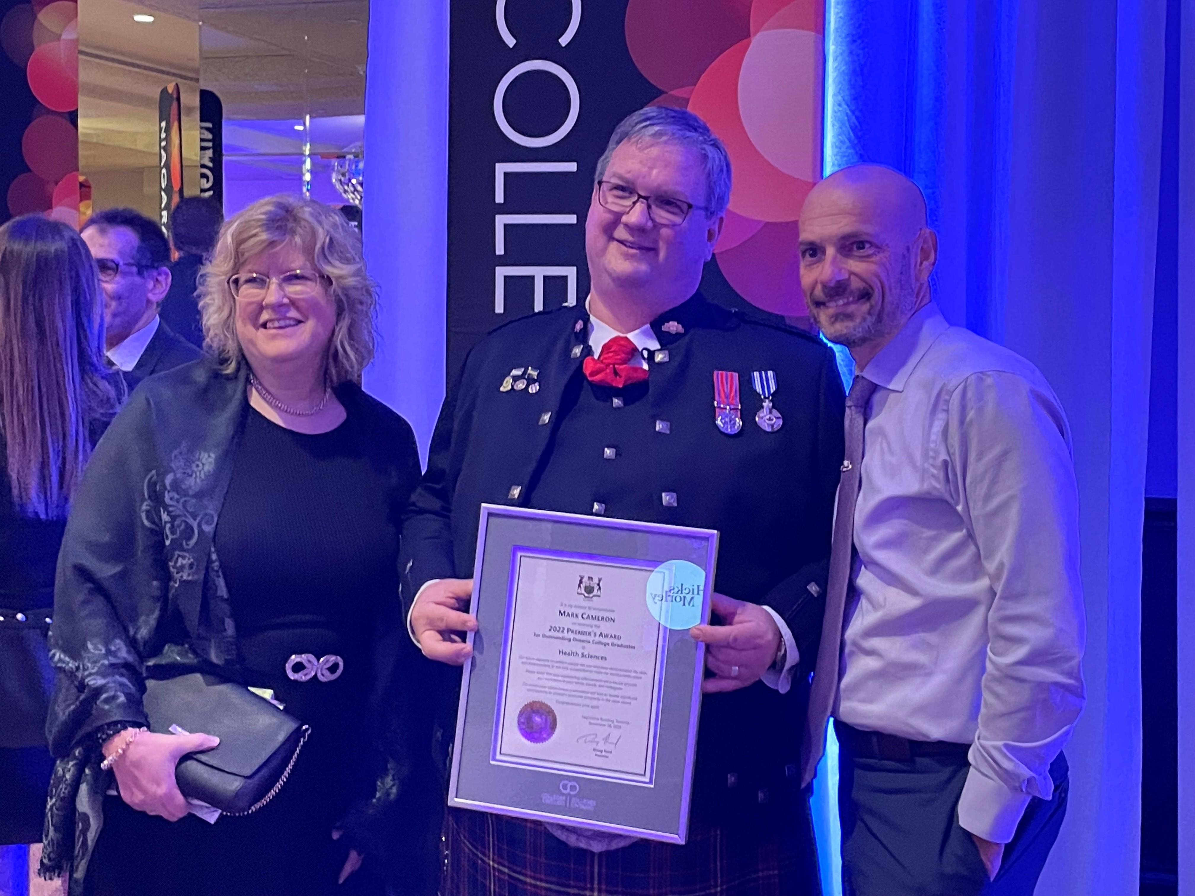 Mark Cameron holds his 2022 Premier’s Award while he poses for a photo with two other people.