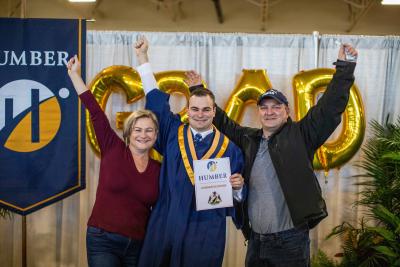 A graduate and their two supporters raise their firsts in celebration at one of the photo booths