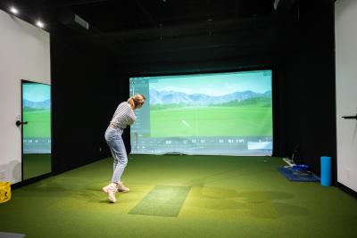 A person swings a golf club on a simulated golf course in front of a digital screen.